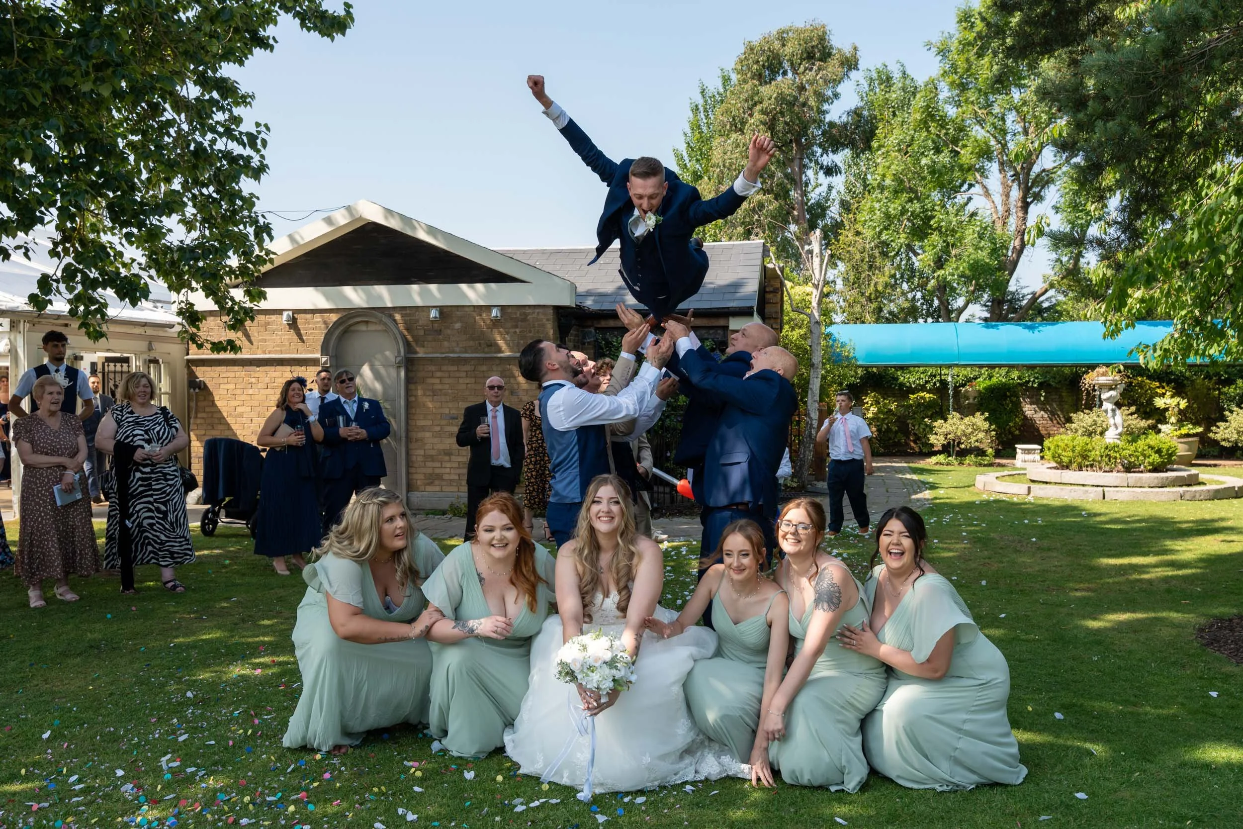 Friern Manor wedding - group shot fun superman throw of the groom with the bridesmaids laughing