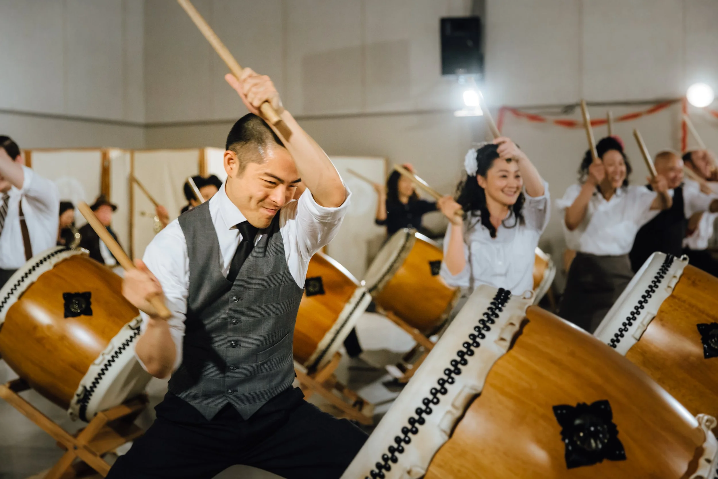 People in swing era clothing joyously hit taiko drums.
