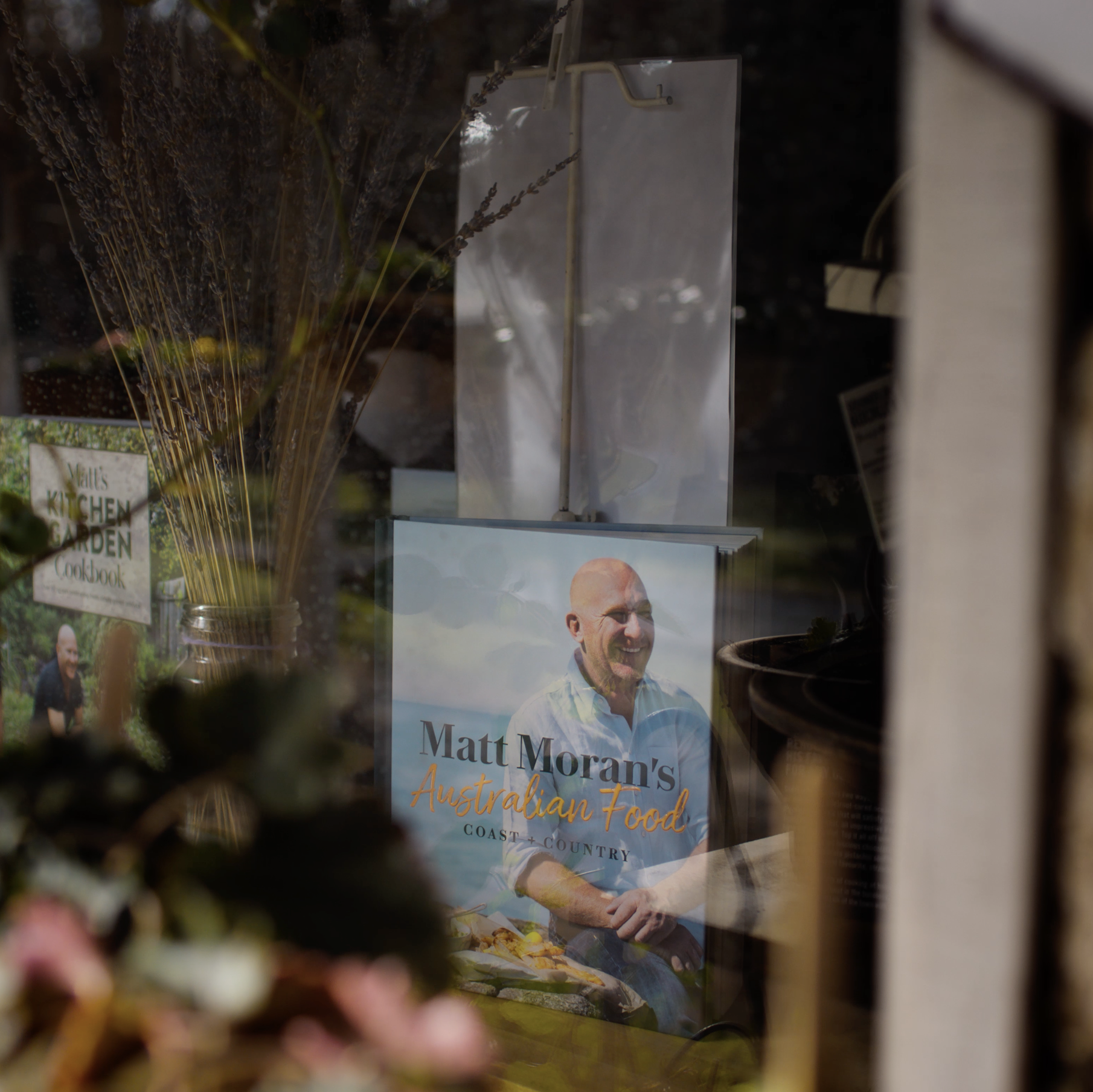 A magazine cover featuring a man with a bald head, smiling, and wearing a white shirt. The magazine titled 'Matt Moran's Australian Food' is partially visible in the foreground. There are dried lavender or similar flowers in the background, along wit