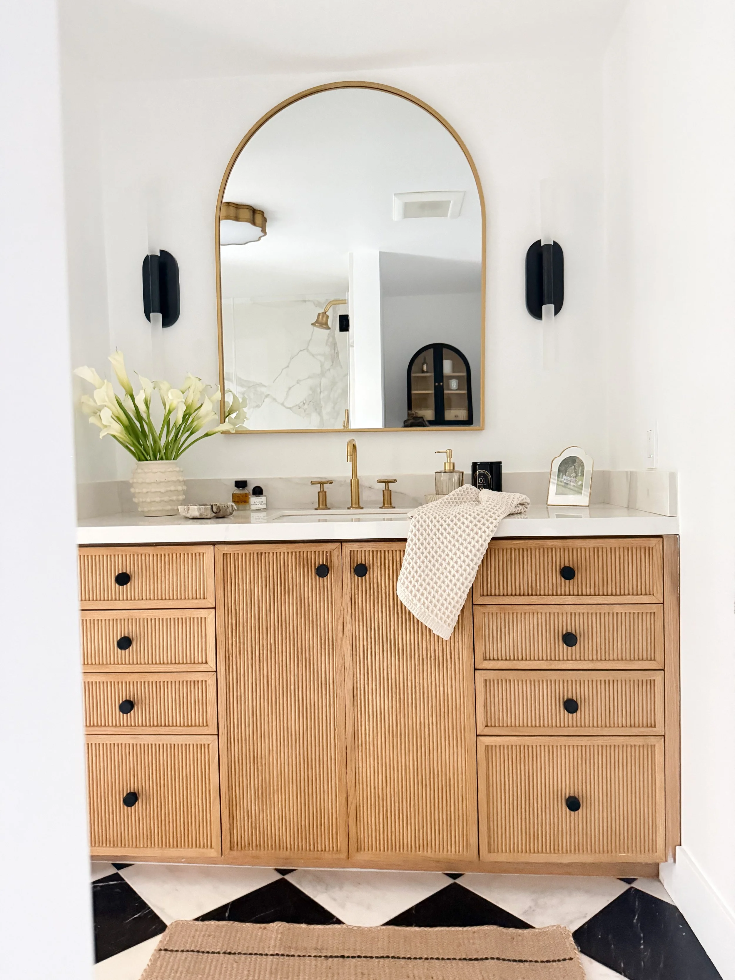 bathroom design, black and white diamond marble tile with custom wood cabinets and arched mirror.