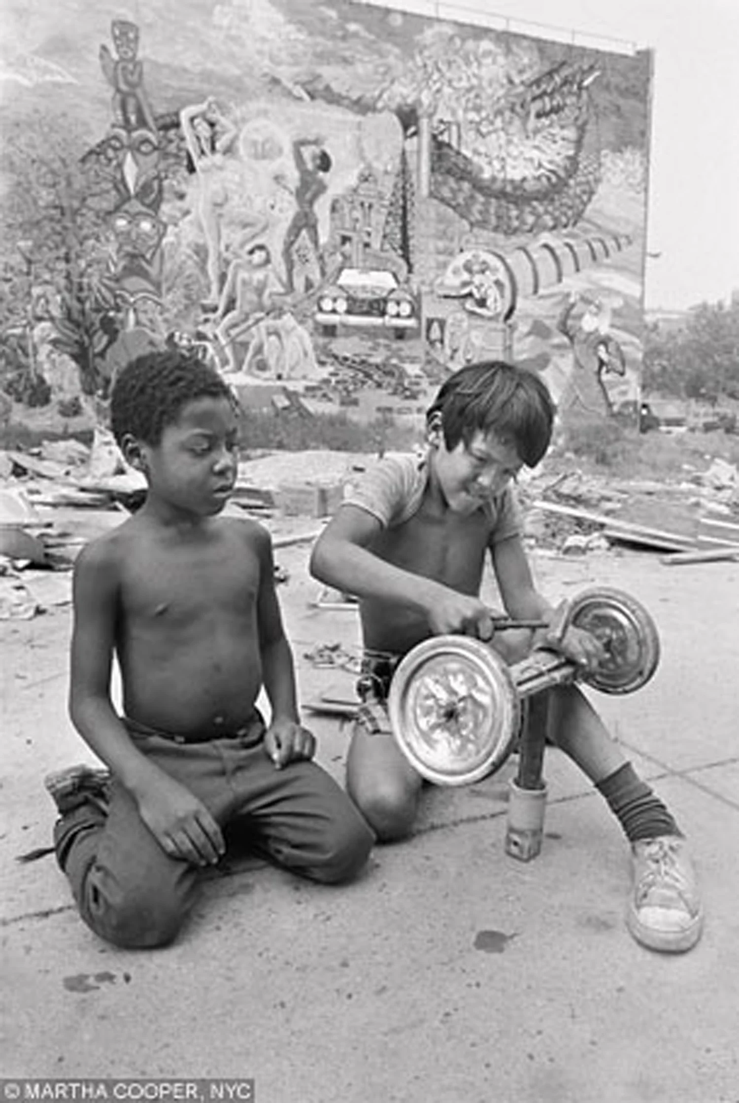 Two children build a go-cart at Rivington Street near Christie. Behind them is New Birth , a 1974 community artists mural directed by Jimmy Jannuzzi. Photo by Martha Cooper