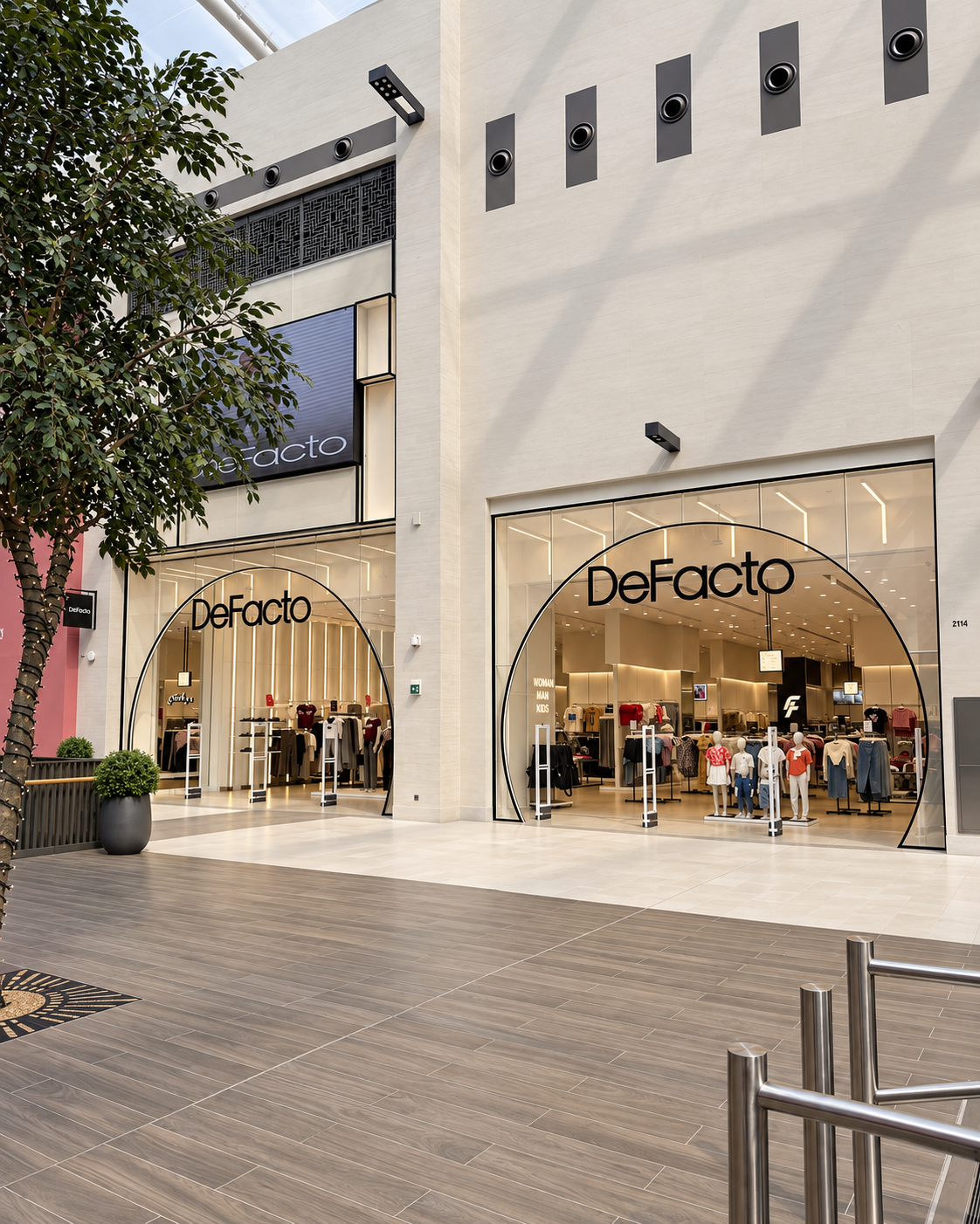 Exterior view of a DeFacto retail store in a shopping mall, with mannequins and clothing displays visible inside, large glass windows, and stylish archway entrances.