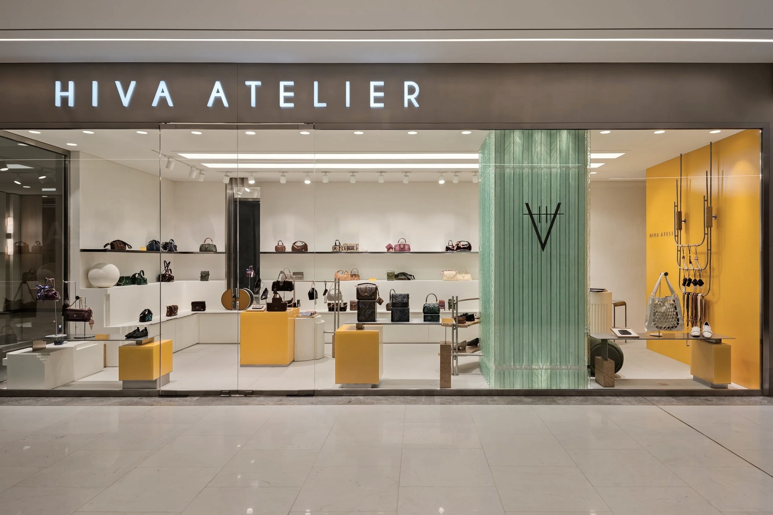 A retail store named HIVA ATELIER selling handbags, shoes, and accessories displayed on shelves, tables, and racks inside a modern shopping mall.