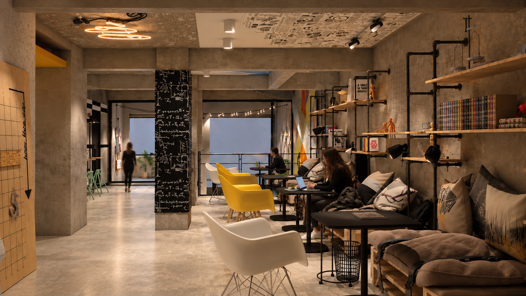 Interior of a modern coffee shop with seating and decorative shelving, people working on laptops, and a person walking in the background.
