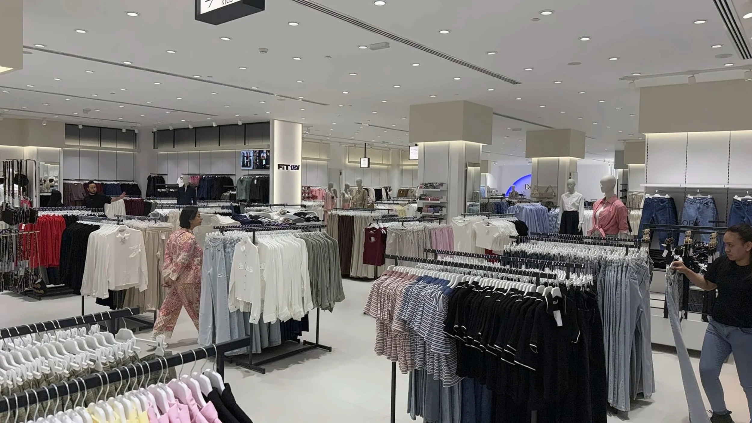 Inside a clothing store with racks of various apparel, mannequins dressed in casual clothes, and shoppers browsing merchandise.