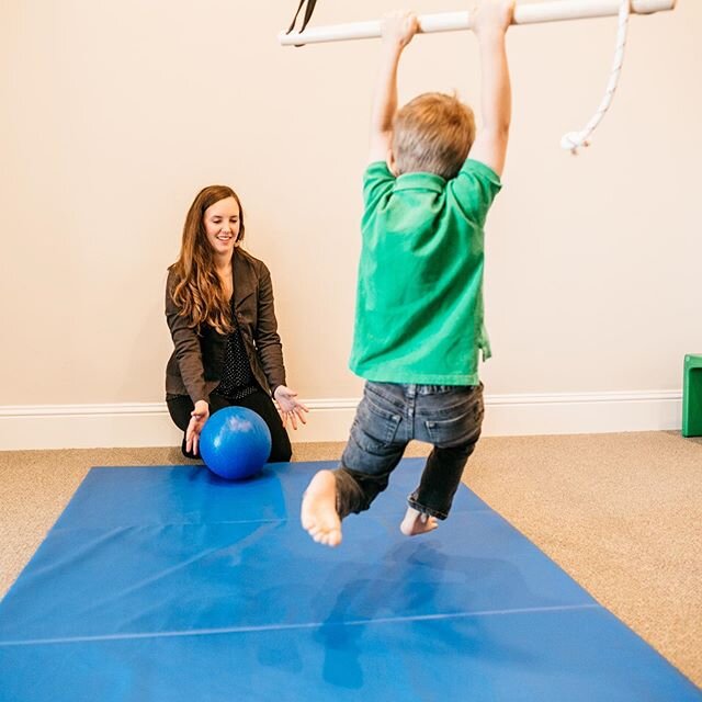 Check out the action captured in this photo! This child is using the trapeze swing to strengthen his upper body which allows his feet to come off the floor. He has gained enough strength to swing himself and kick a ball back to Jamie.⠀
⠀
This activit