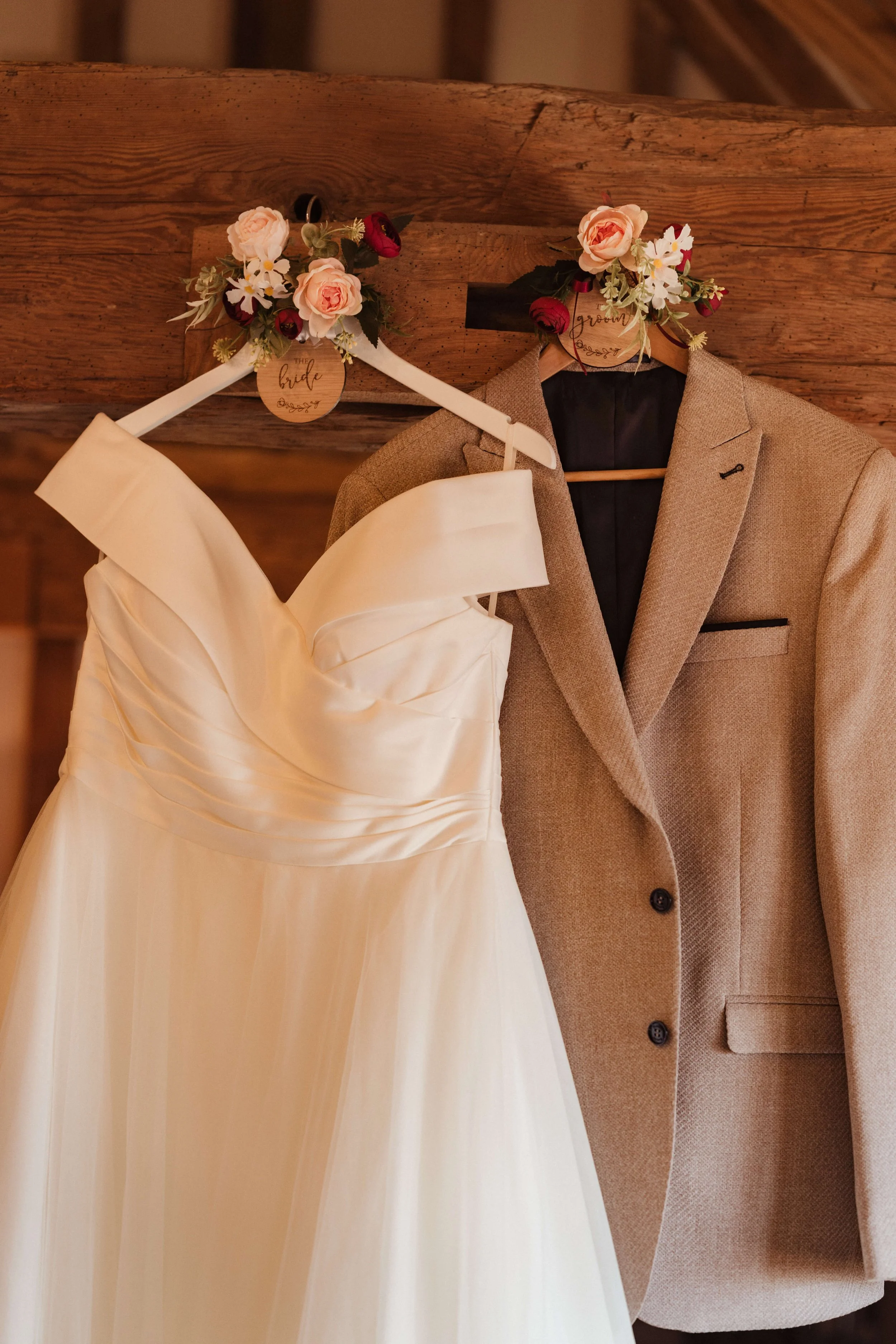 A wedding dress and a groom's suit hanging on wooden hooks decorated with floral arrangements, labeled 'bride' and 'groom'.