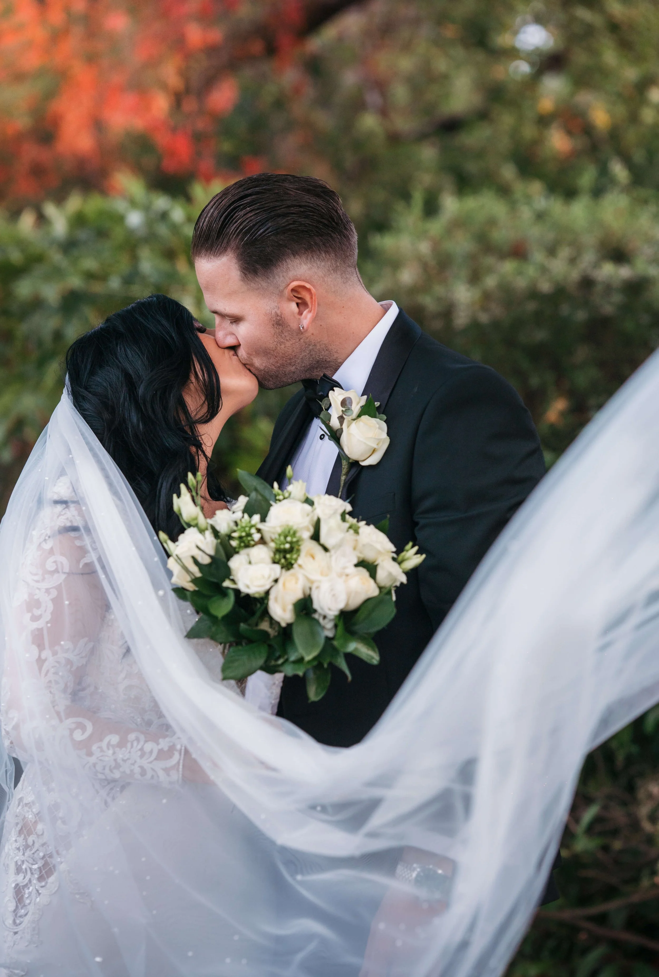 bride and groom kissing with veil blowing in the wind a very romantic soft lit photograph