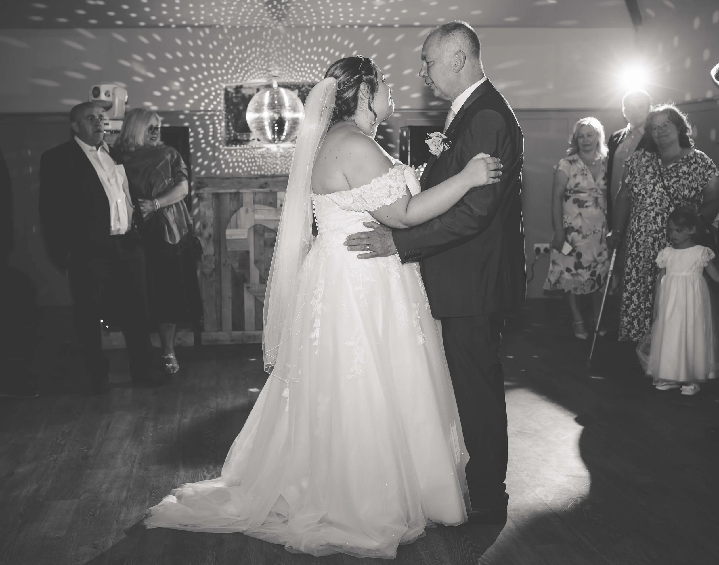 A bride and groom sharing their first dance at a wedding reception, surrounded by guests on the dance floor.