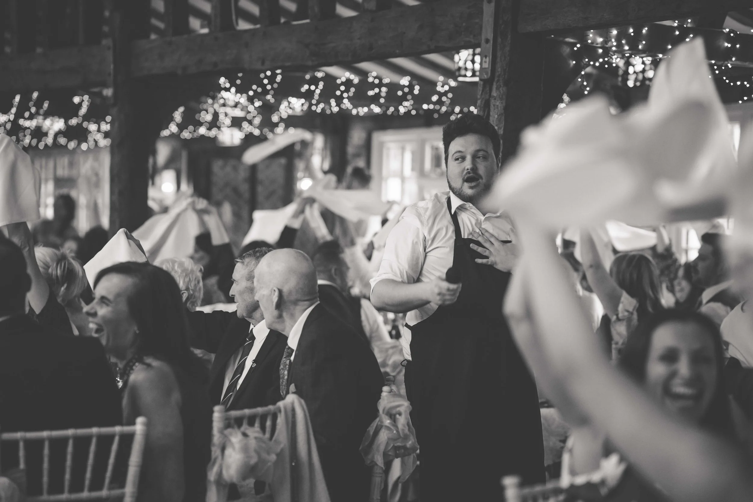 guests wave serviettes whilst waiter sings to wedding guests