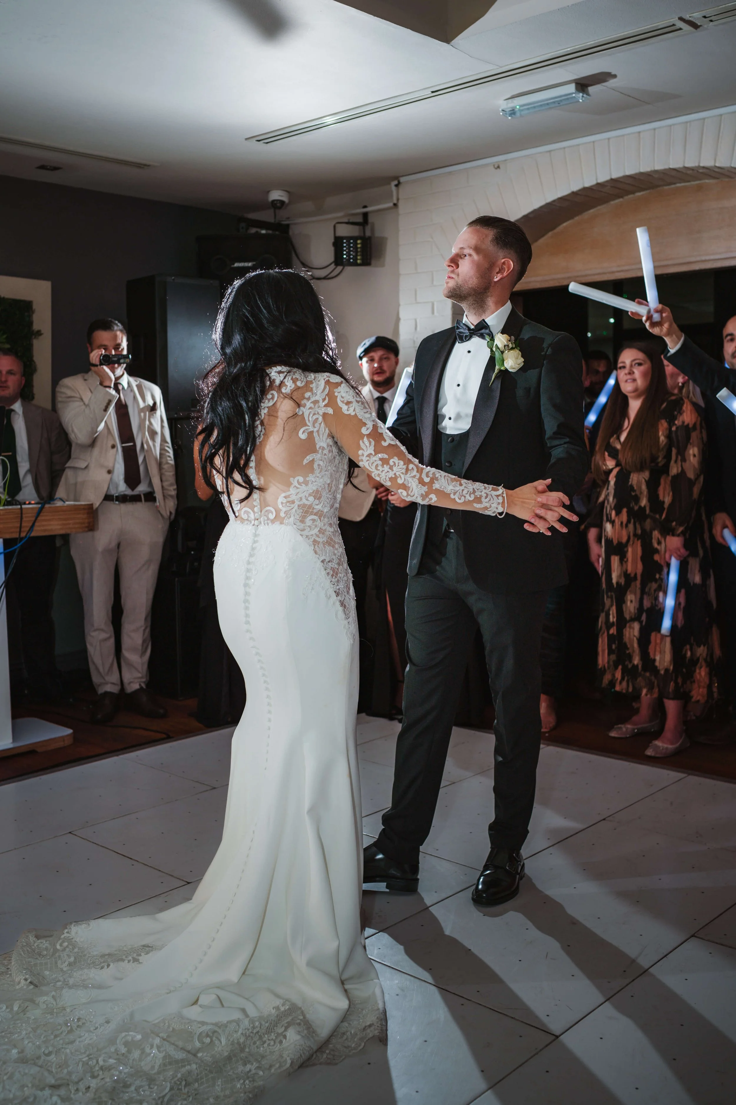 A bride and groom dance together at their wedding reception, surrounded by guests.