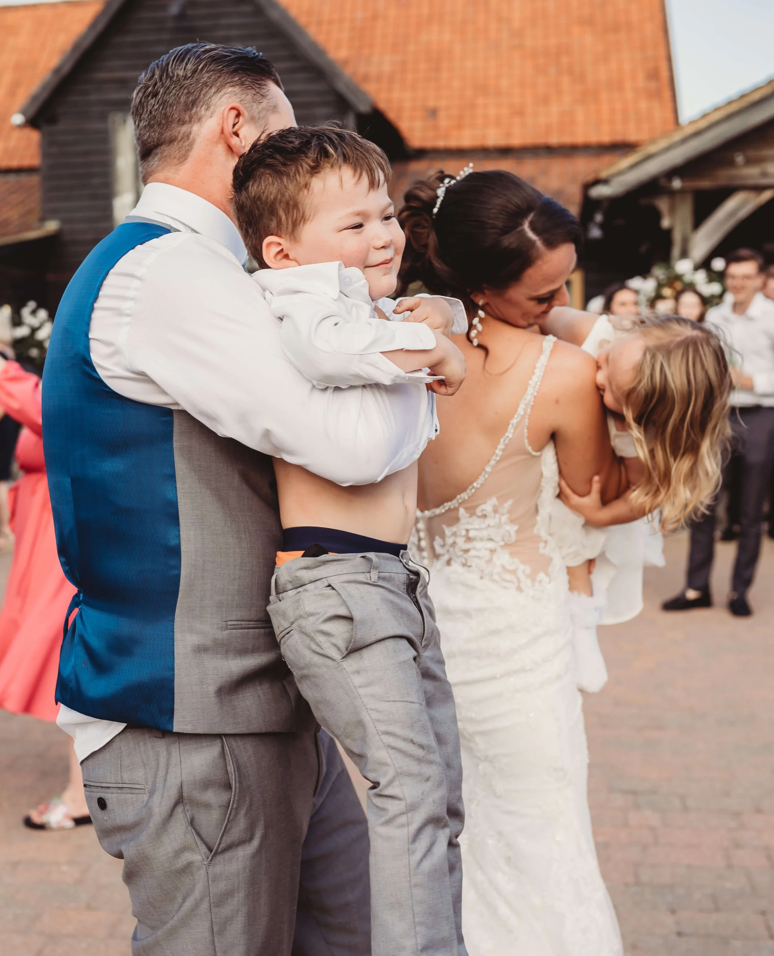 A man holding a young boy, a woman in a wedding dress, and a young girl at an outdoor wedding reception.
