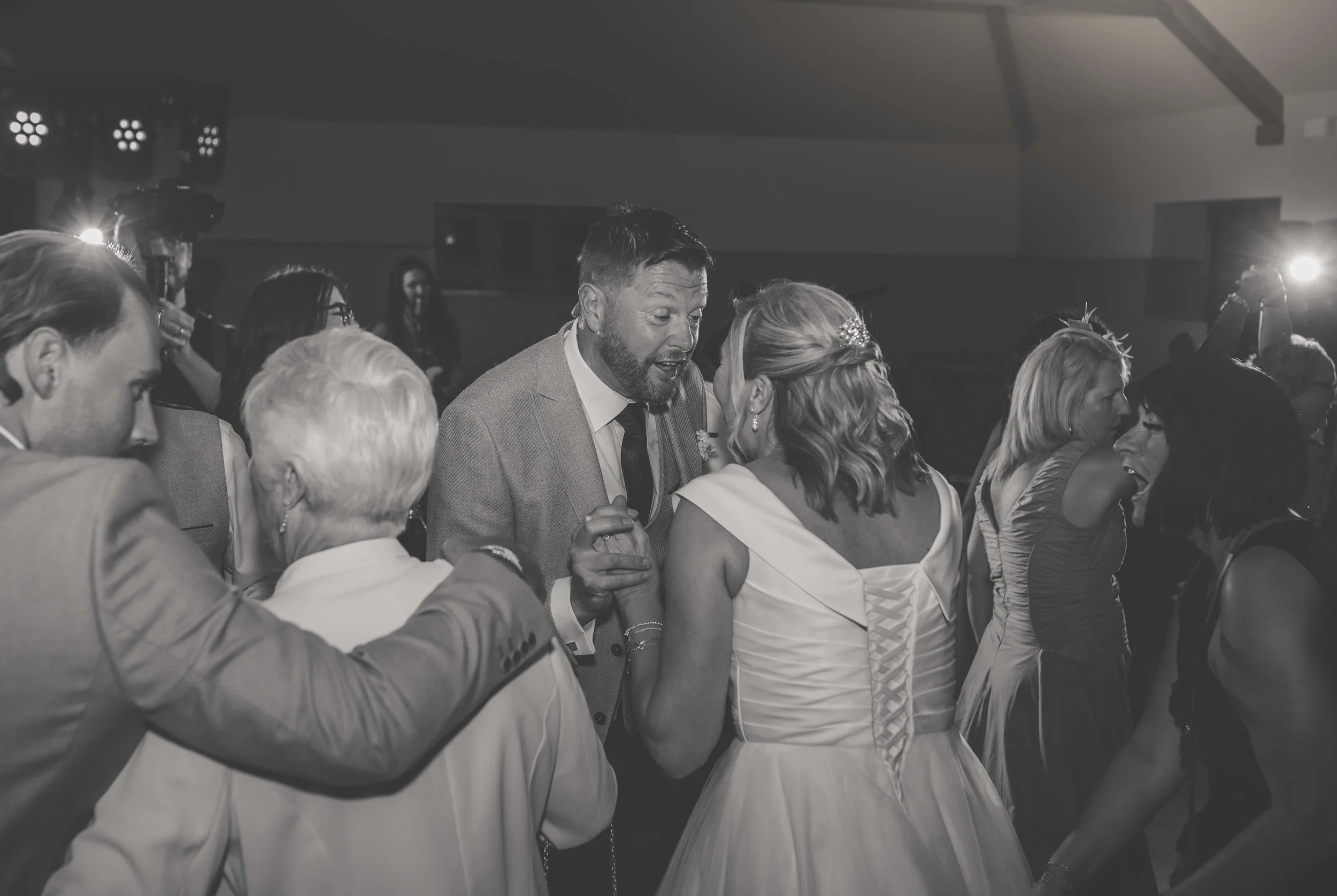 People dancing and celebrating at a wedding reception in a dimly lit venue.