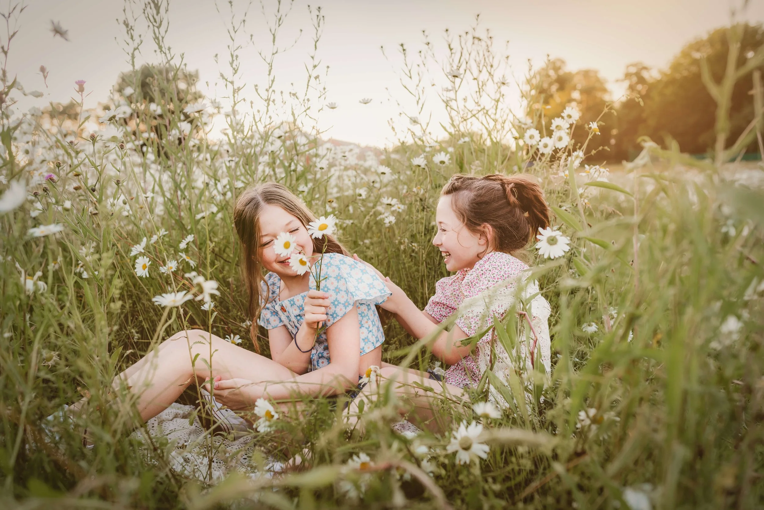 Two young girls enjoying a sunny day in a field of daisies, laughing and playing together.
