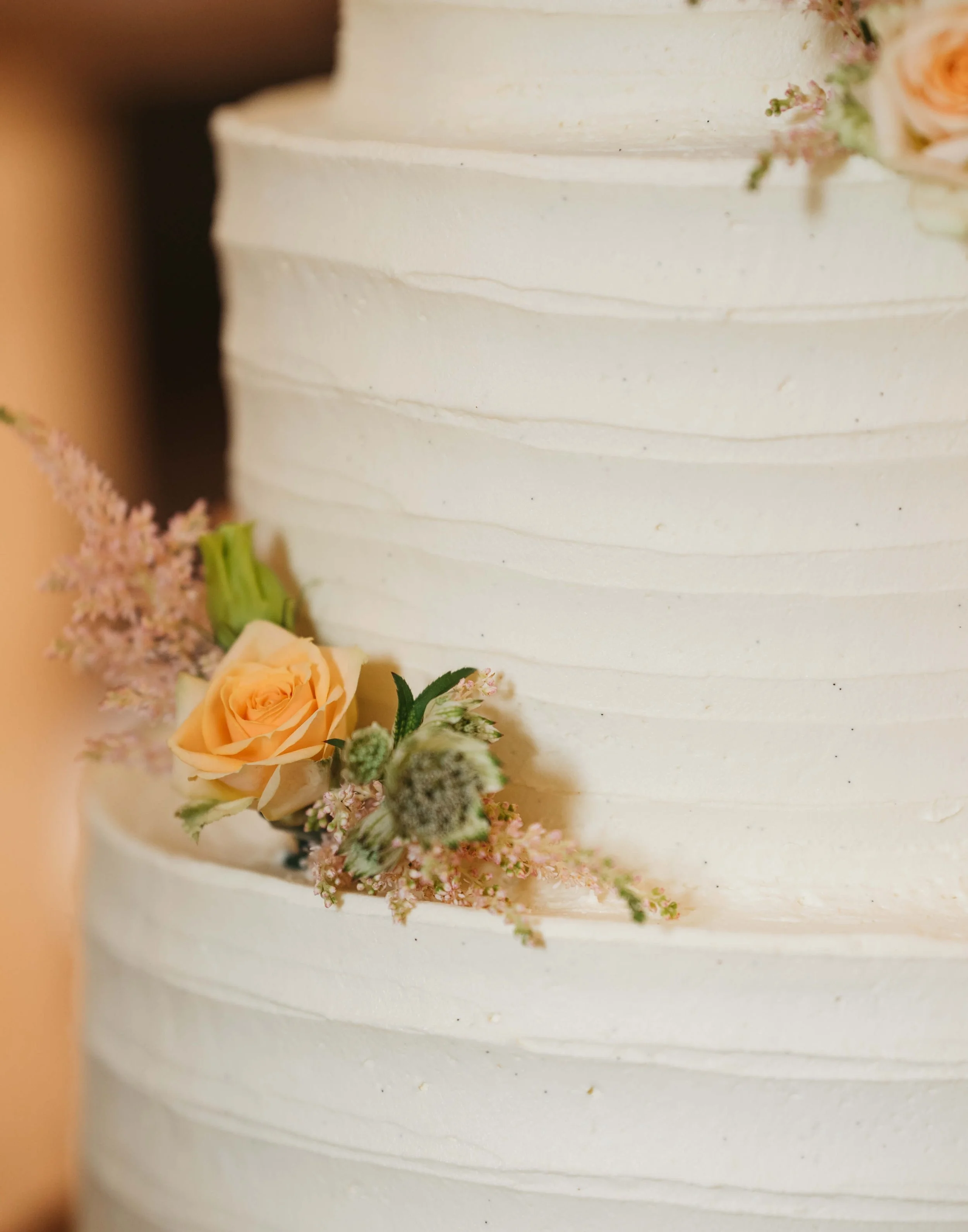 Close-up of a wedding cake decorated with peach roses and pink and green flowers.