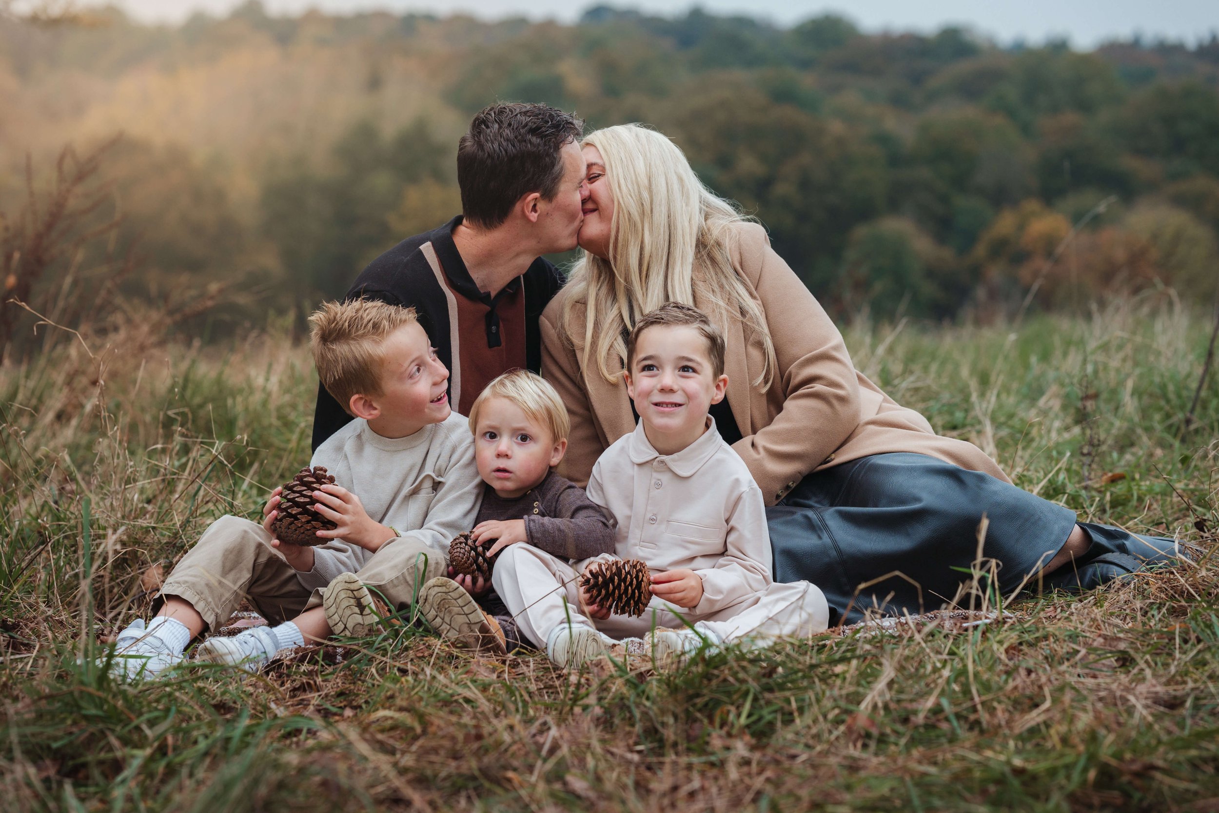 family posing for photo session with mum and dad kissing, in a woodland autumnal back drop of essex