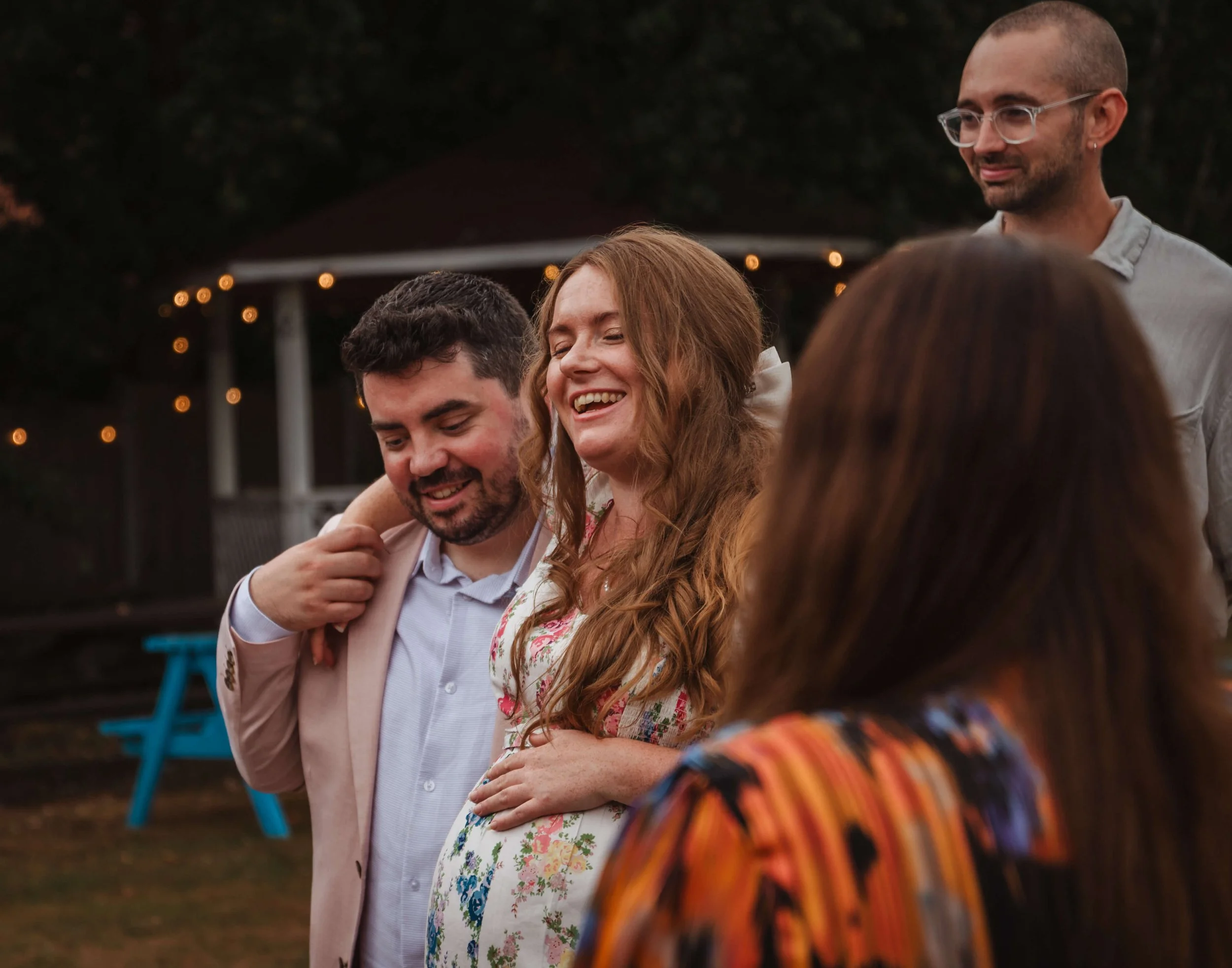 Happy people enjoying an outdoor gathering at sunset, with warm lighting and a gazebo in the background.