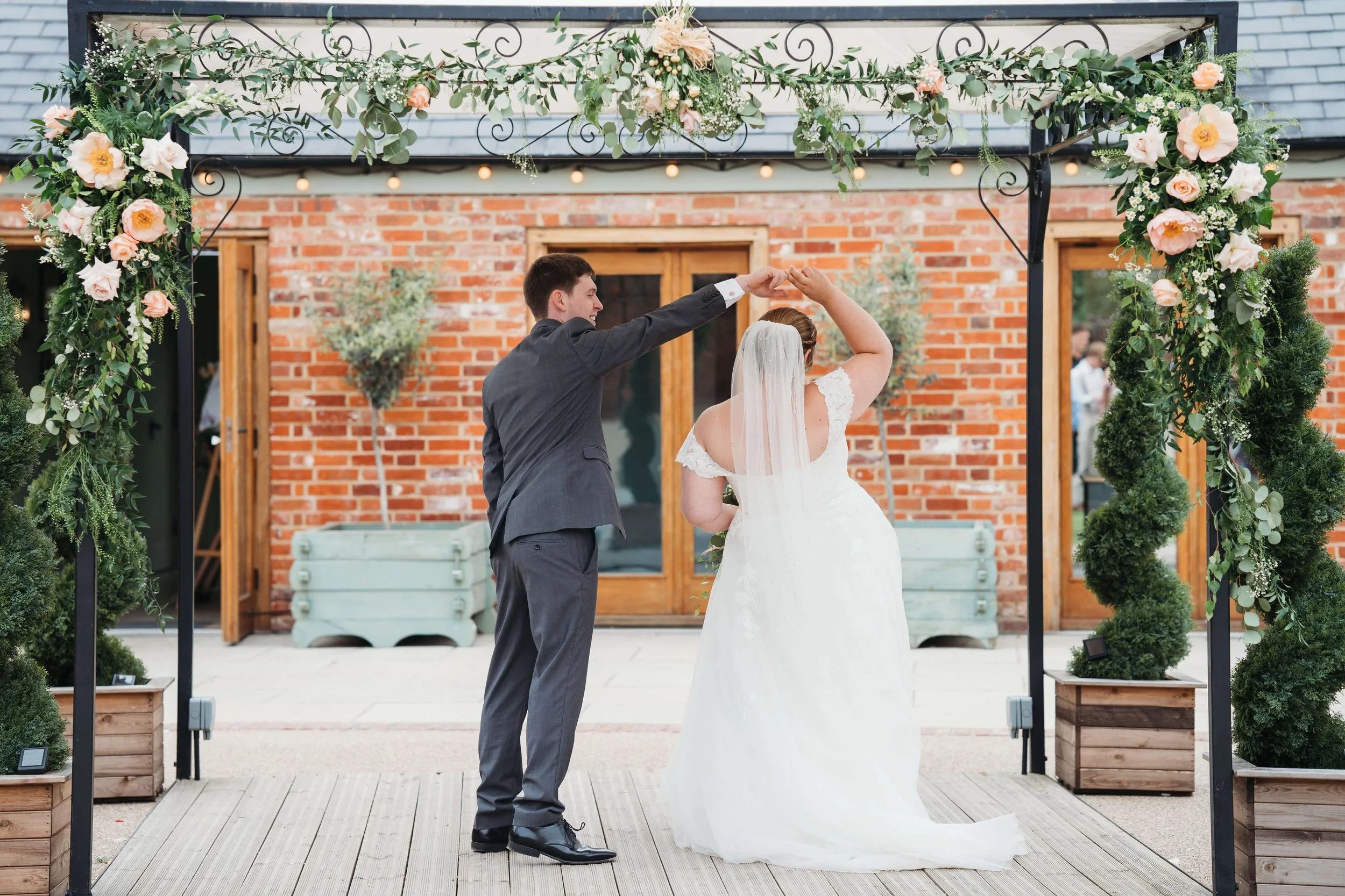 A bride and groom dancing under a decorated outdoor arch at their wedding celebration.