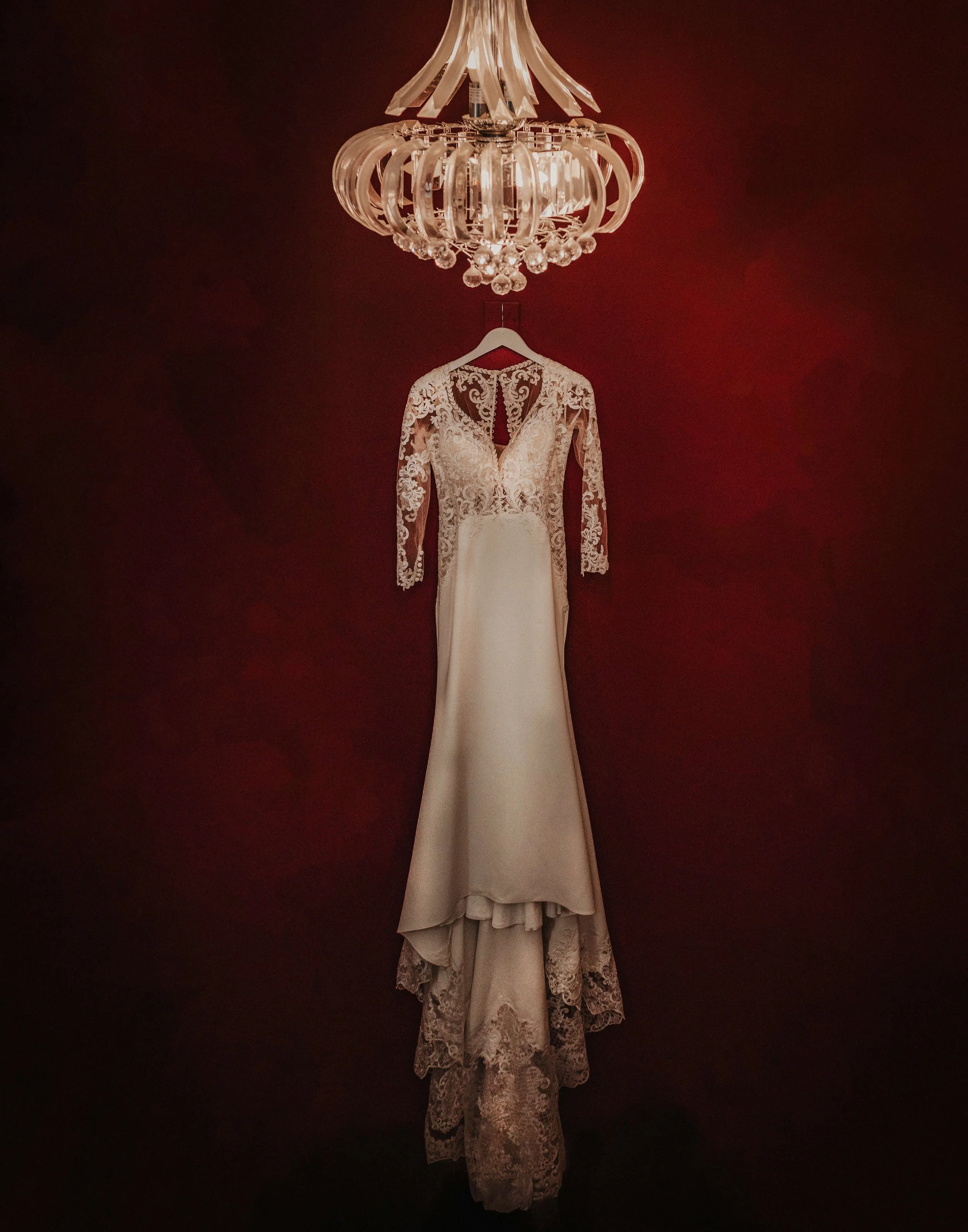 artistic photograph of wedding bridal gown hanging in dark area lit up by chandelier