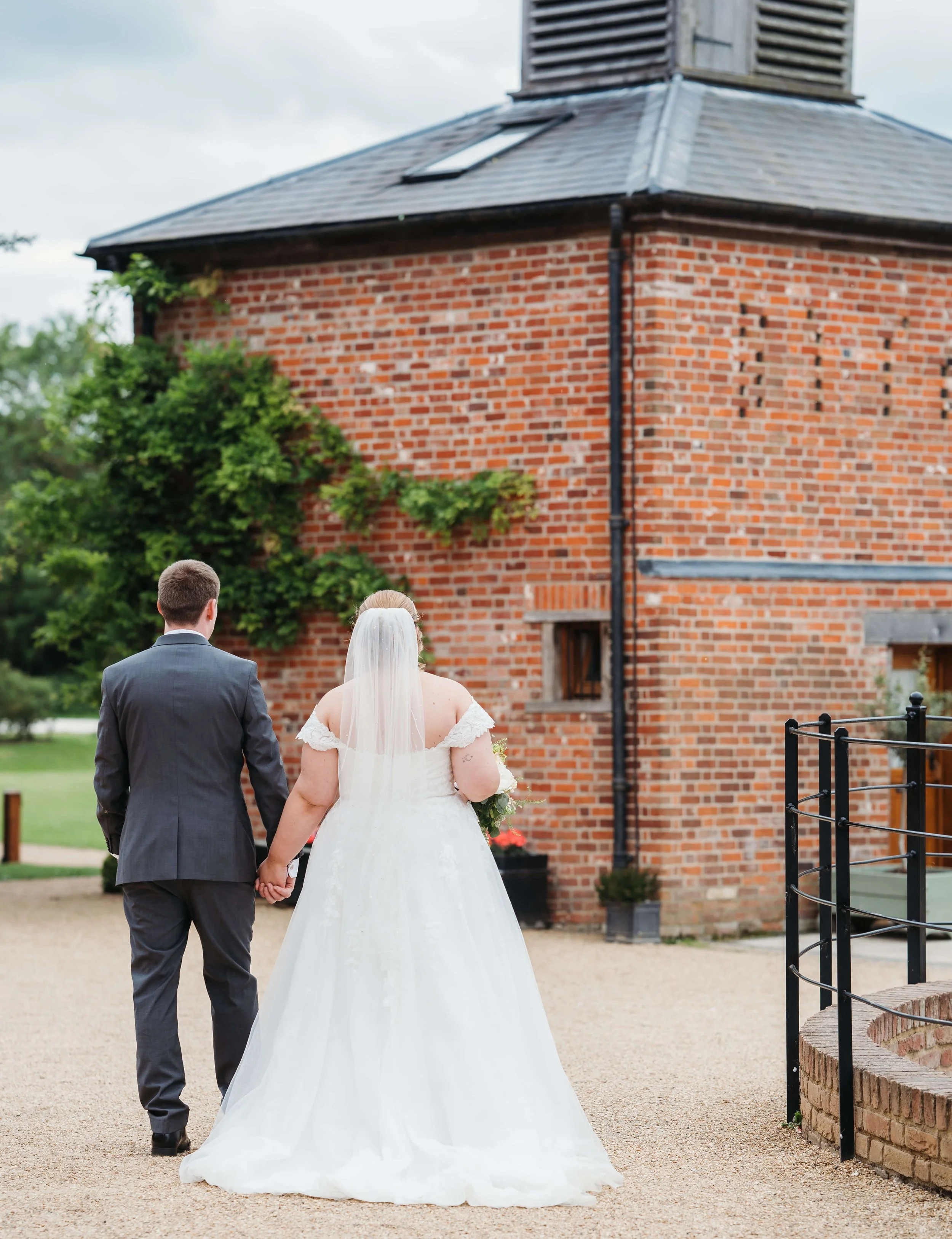 A bride and groom holding hands and walking away from the camera outside near a brick building during a wedding ceremony.