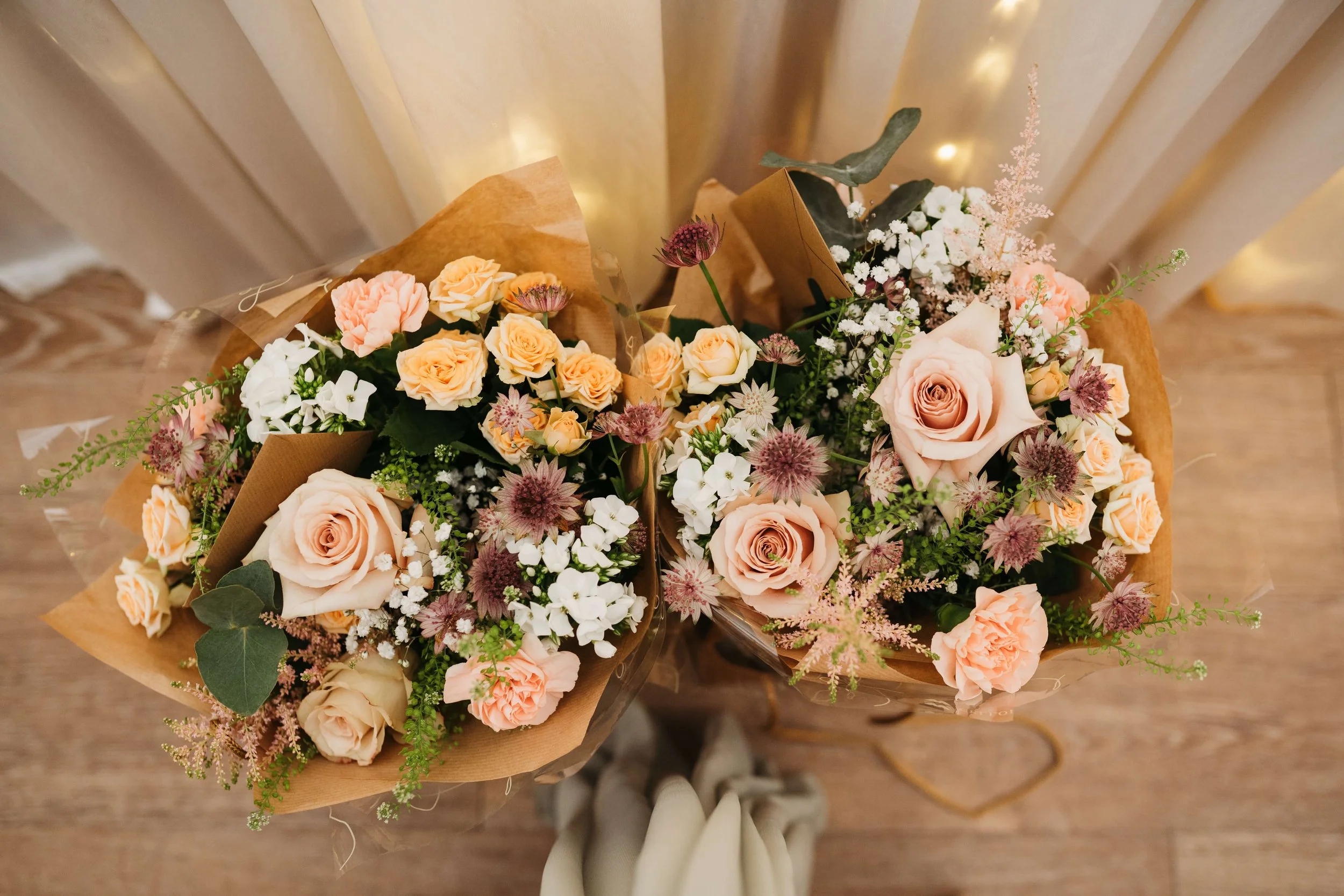 Two bouquets of peach and white roses, pink carnations, baby's breath, and other greenery.