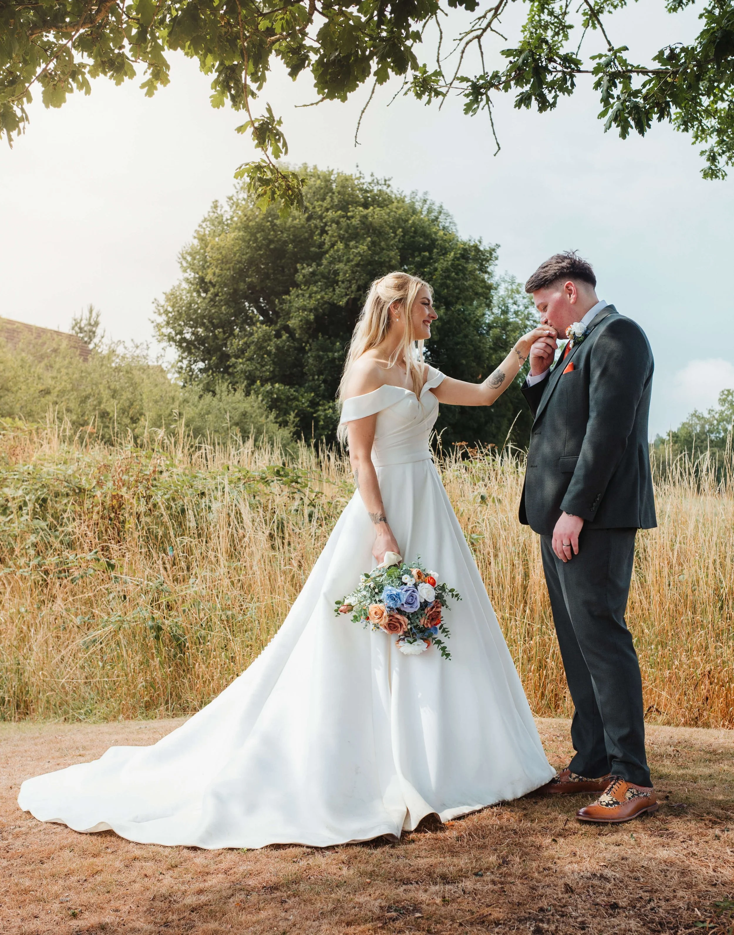 groom kisses brides hand under tree at golden hour 