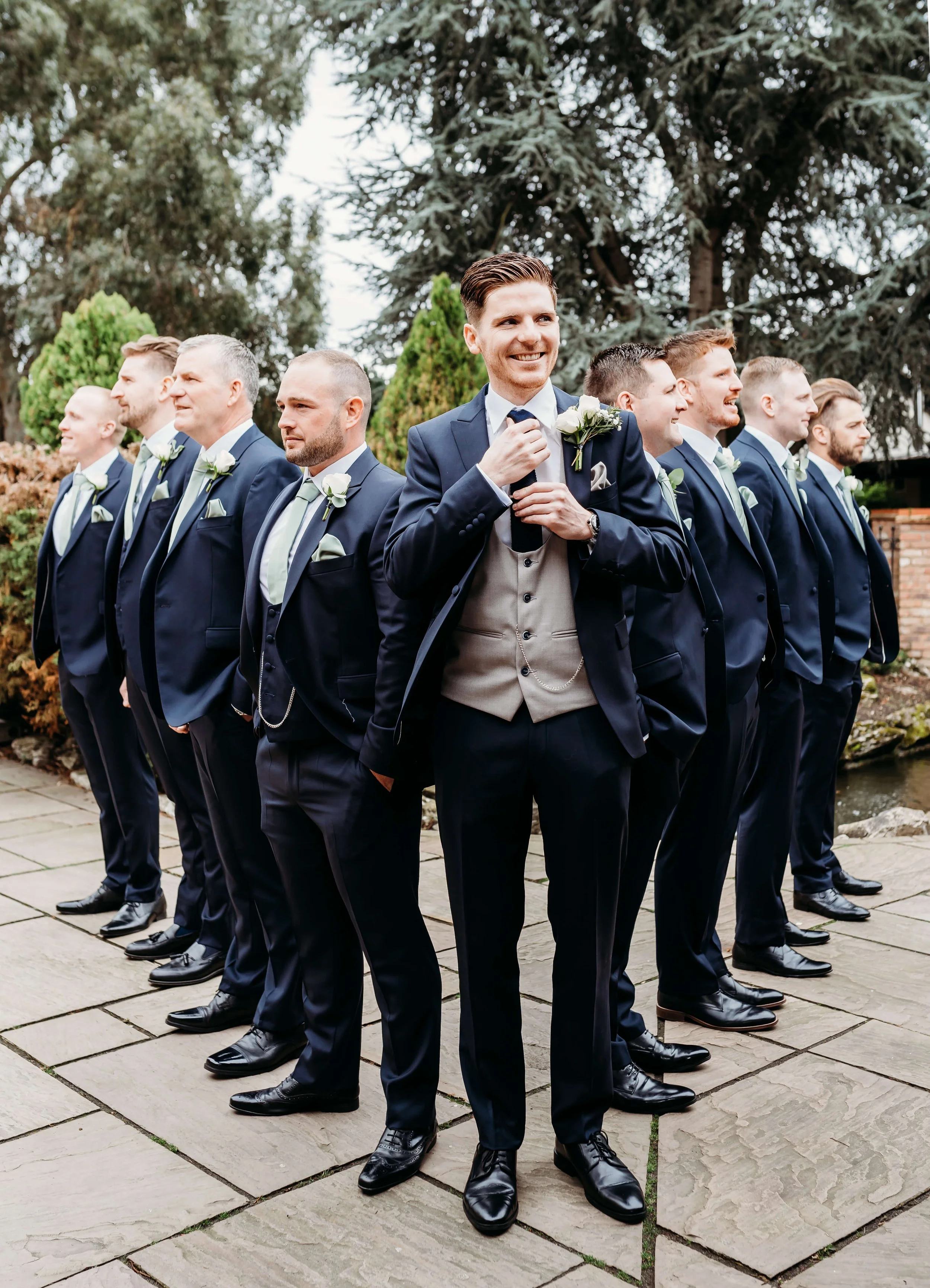 Groom and his groomsmen all stand in a triangle pose whilst groom checks his tie at ye old plough Essex