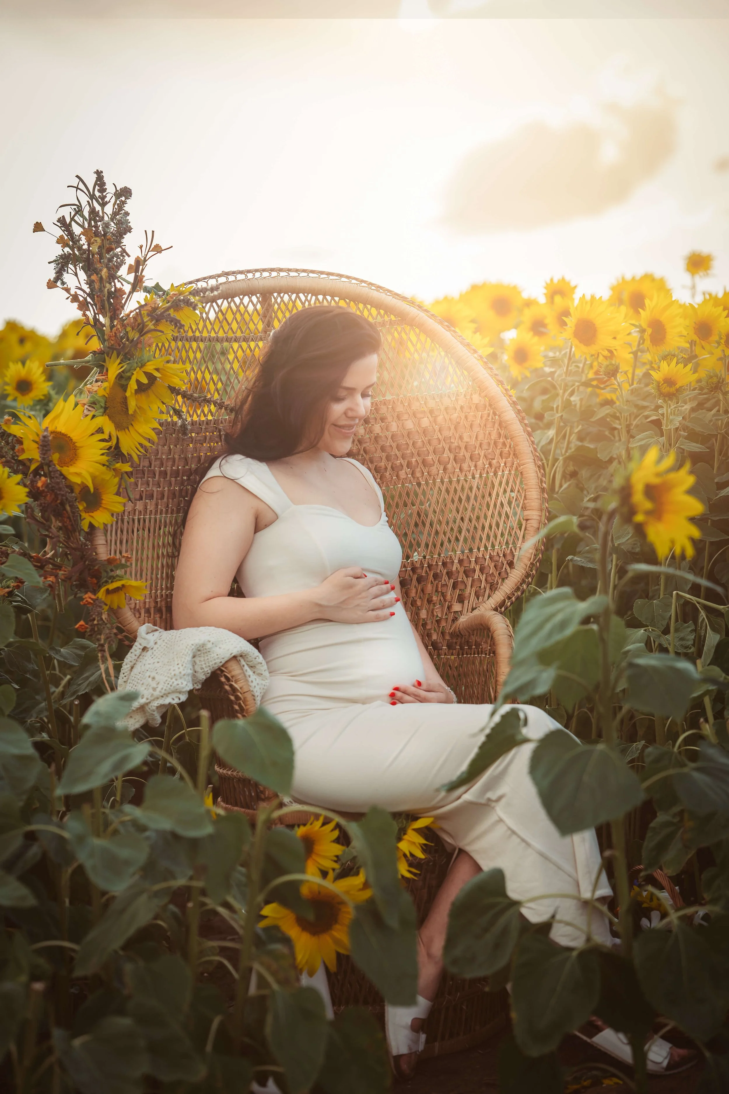 mum holding belly in peacock chair at the golden hour 