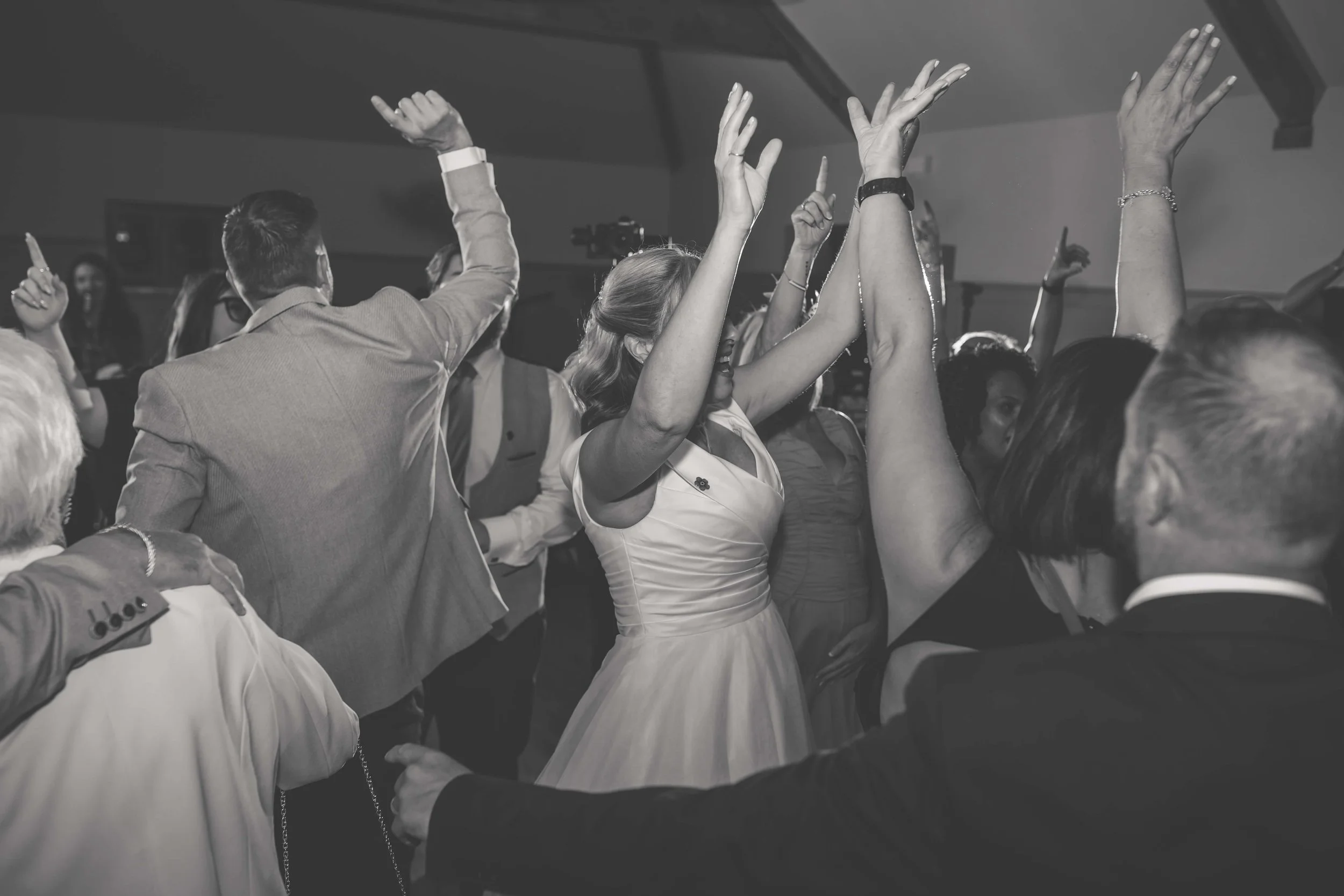 Black and white photo of people dancing and raising their hands at a celebration or party.