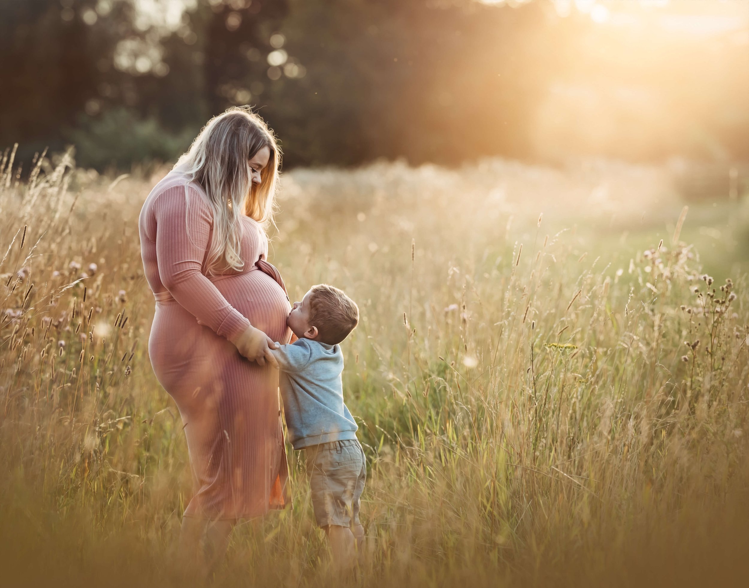 sin kisses mums pregnant belly in field at golden hour 