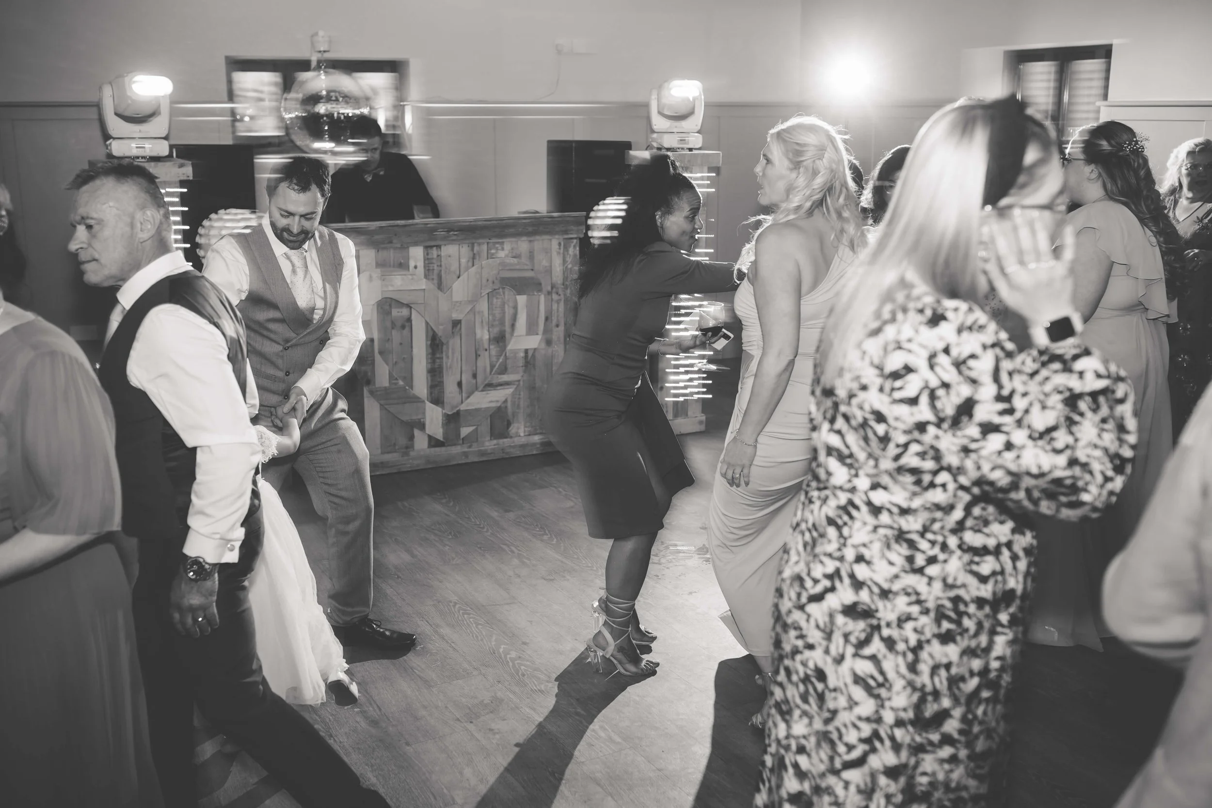 People dancing and socializing at a party in a venue with a wooden bar in the background, black and white photo.