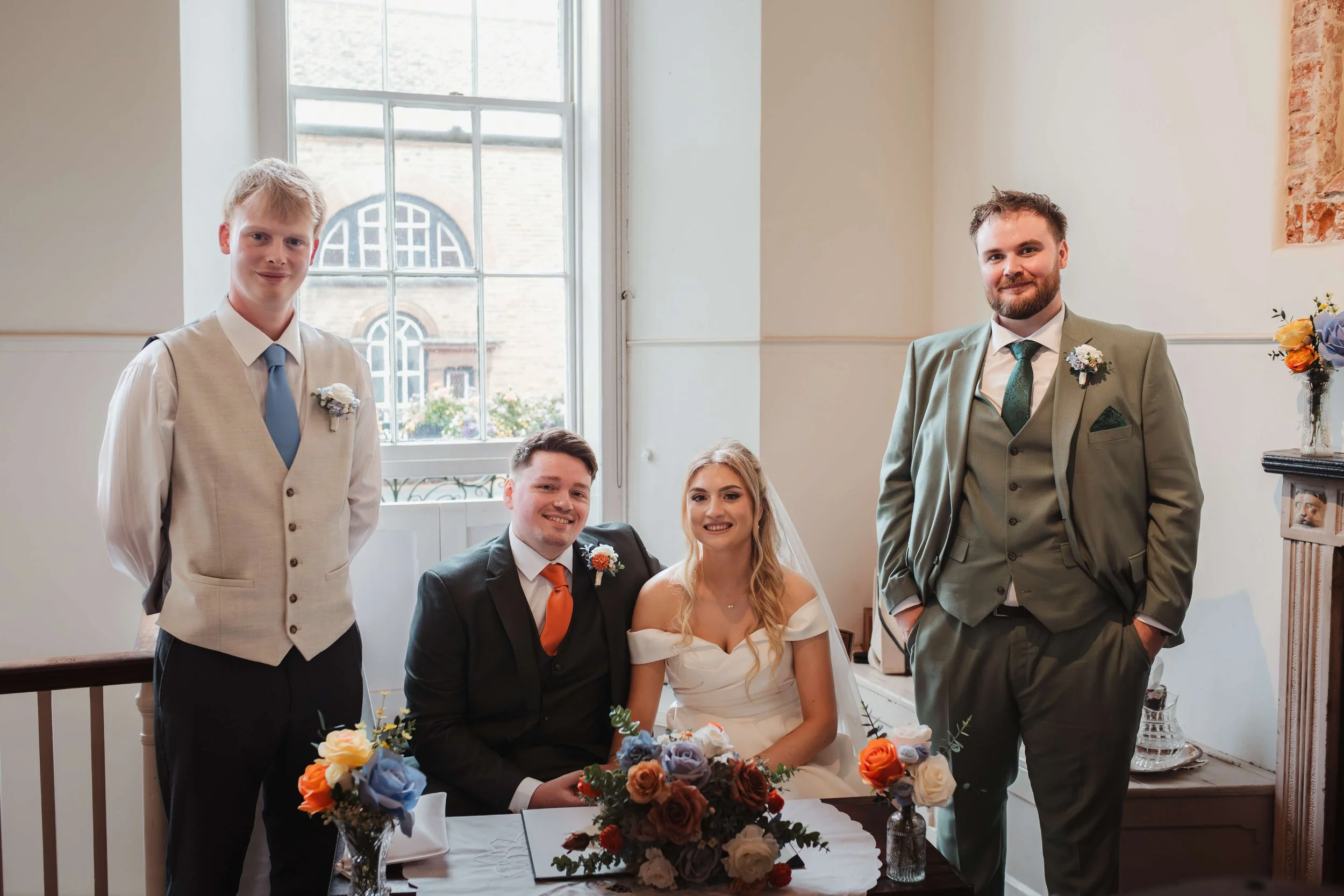 Wedding celebration with the bride, groom, and three male attendants inside a decorated room.