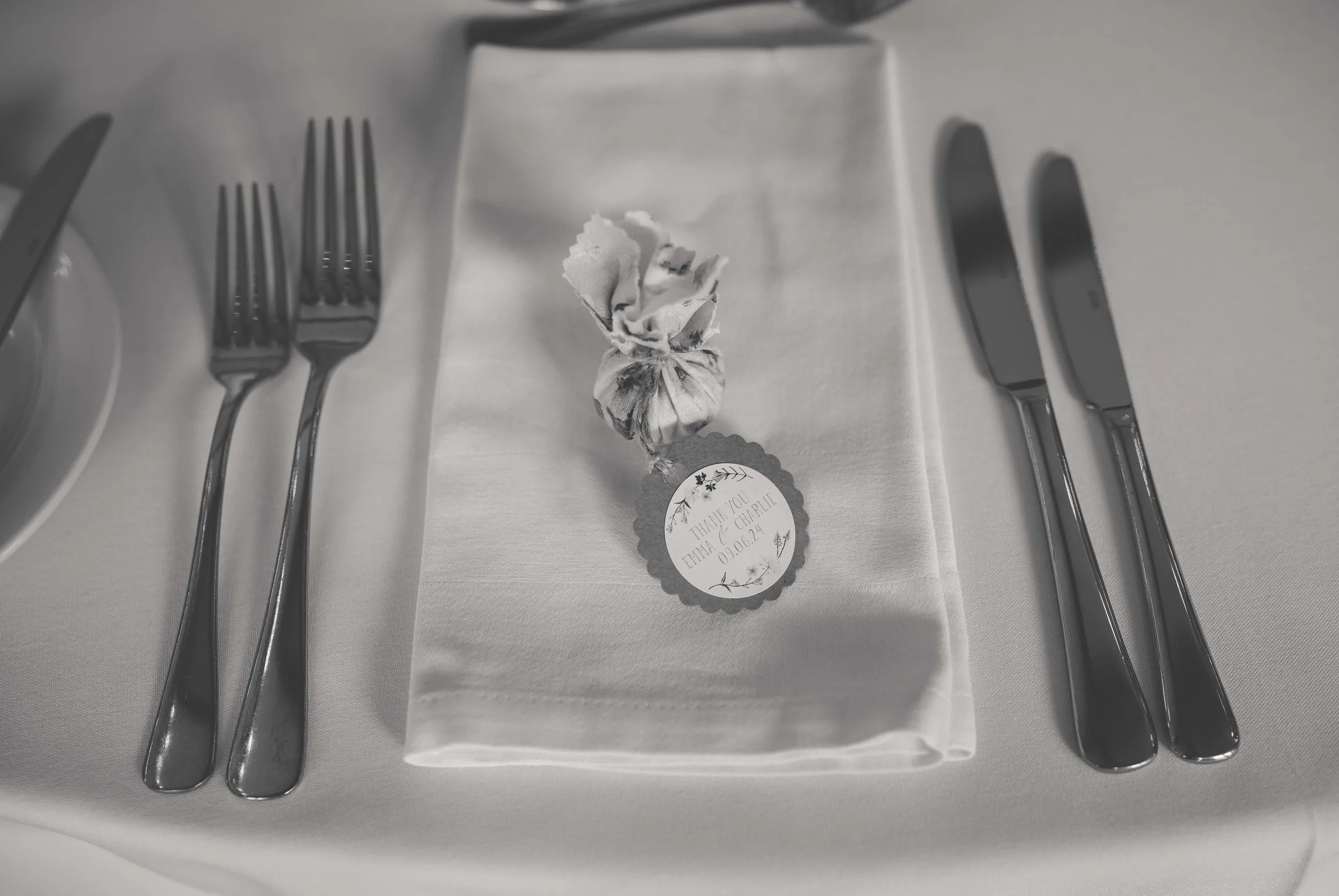 A napkin with a wrapped favor and a thank you tag placed on a neatly set table with silverware.