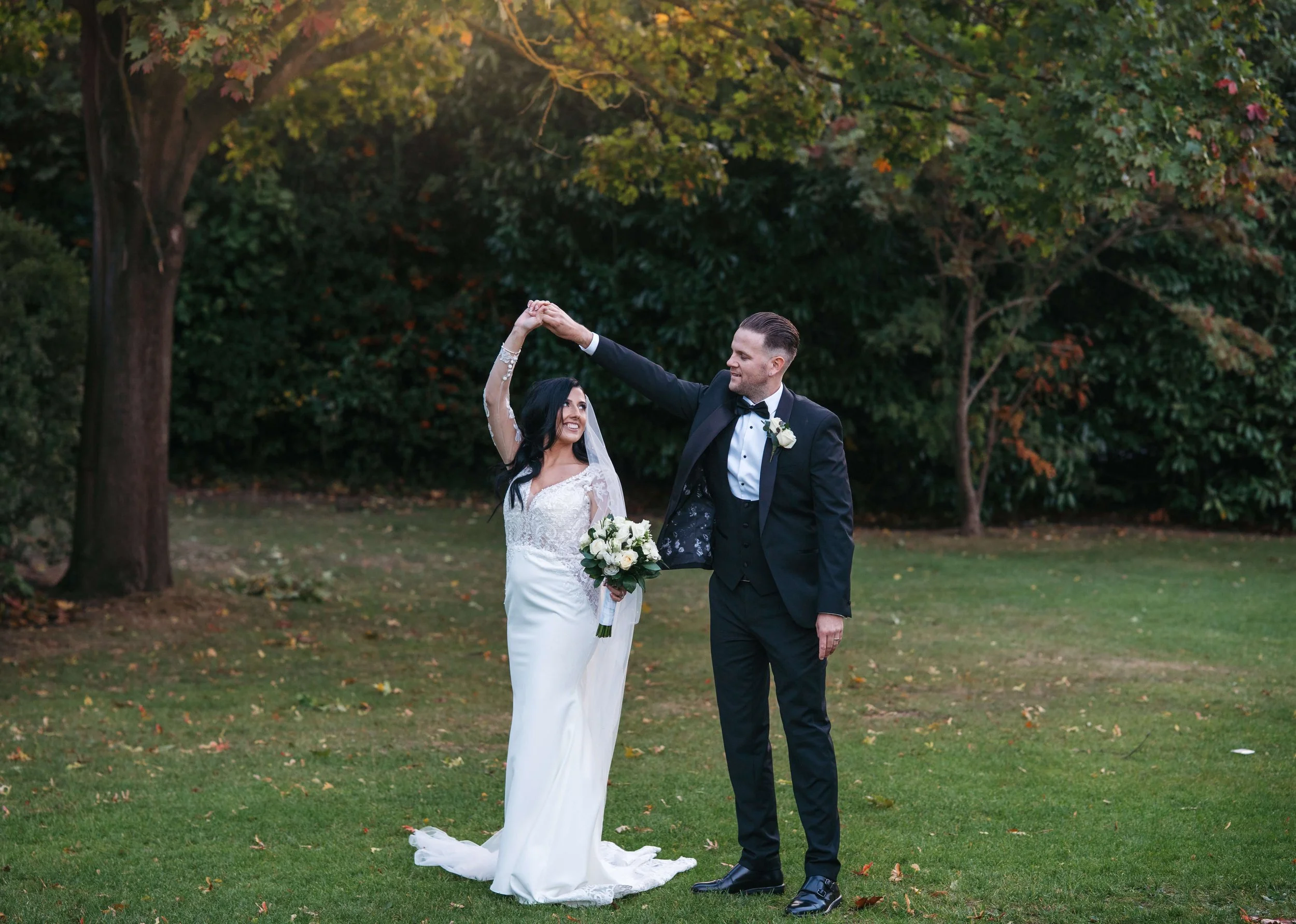 A bride and groom dancing outdoors on a grassy area with trees in the background, during their wedding.