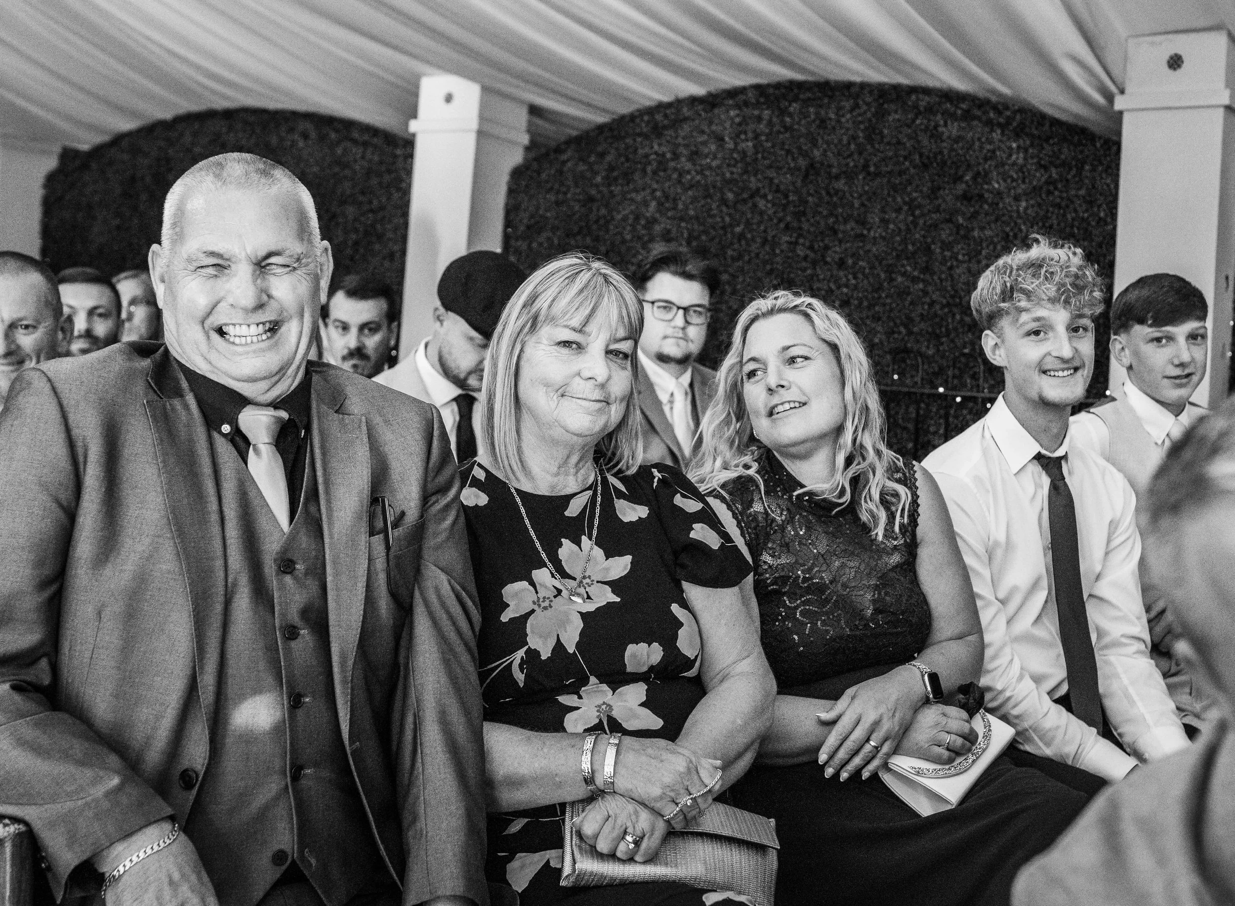 Group of people sitting at an event, smiling and dressed in formal attire, in a decorated indoor setting.