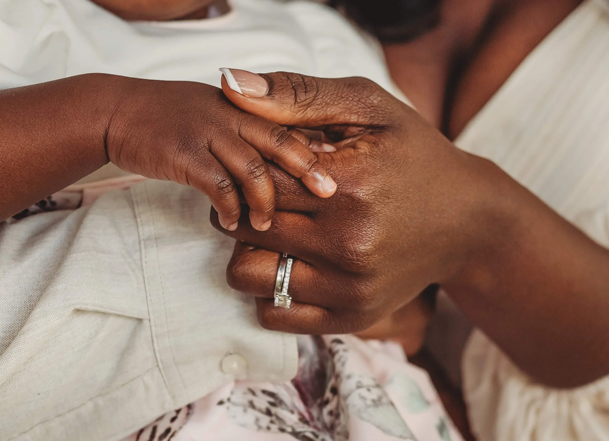 Close-up of a child's hand gently holding an adult's hand, showing a wedding ring on the adult's finger.