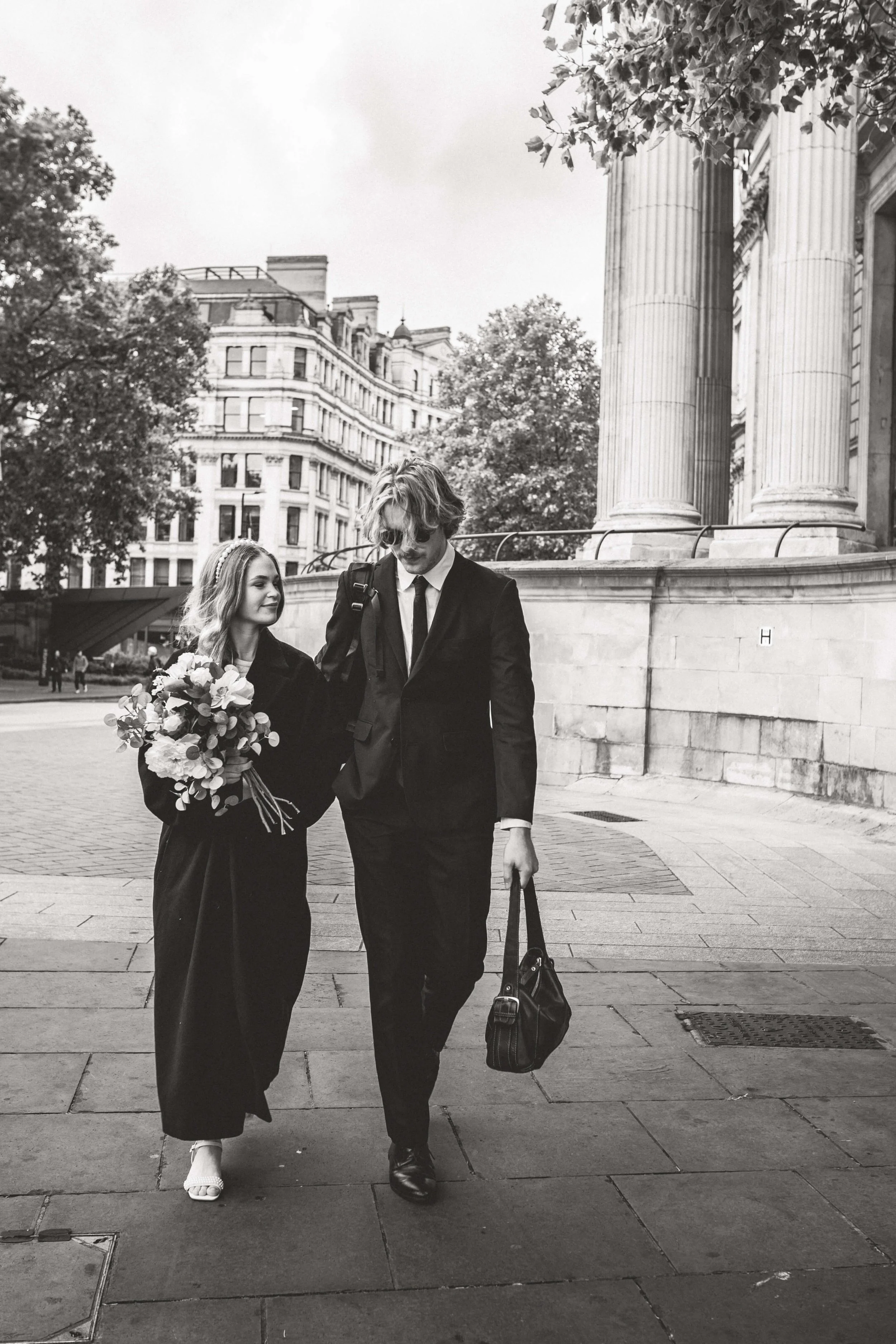 Groom carries Brides Handbag whilst she wears his coat in London