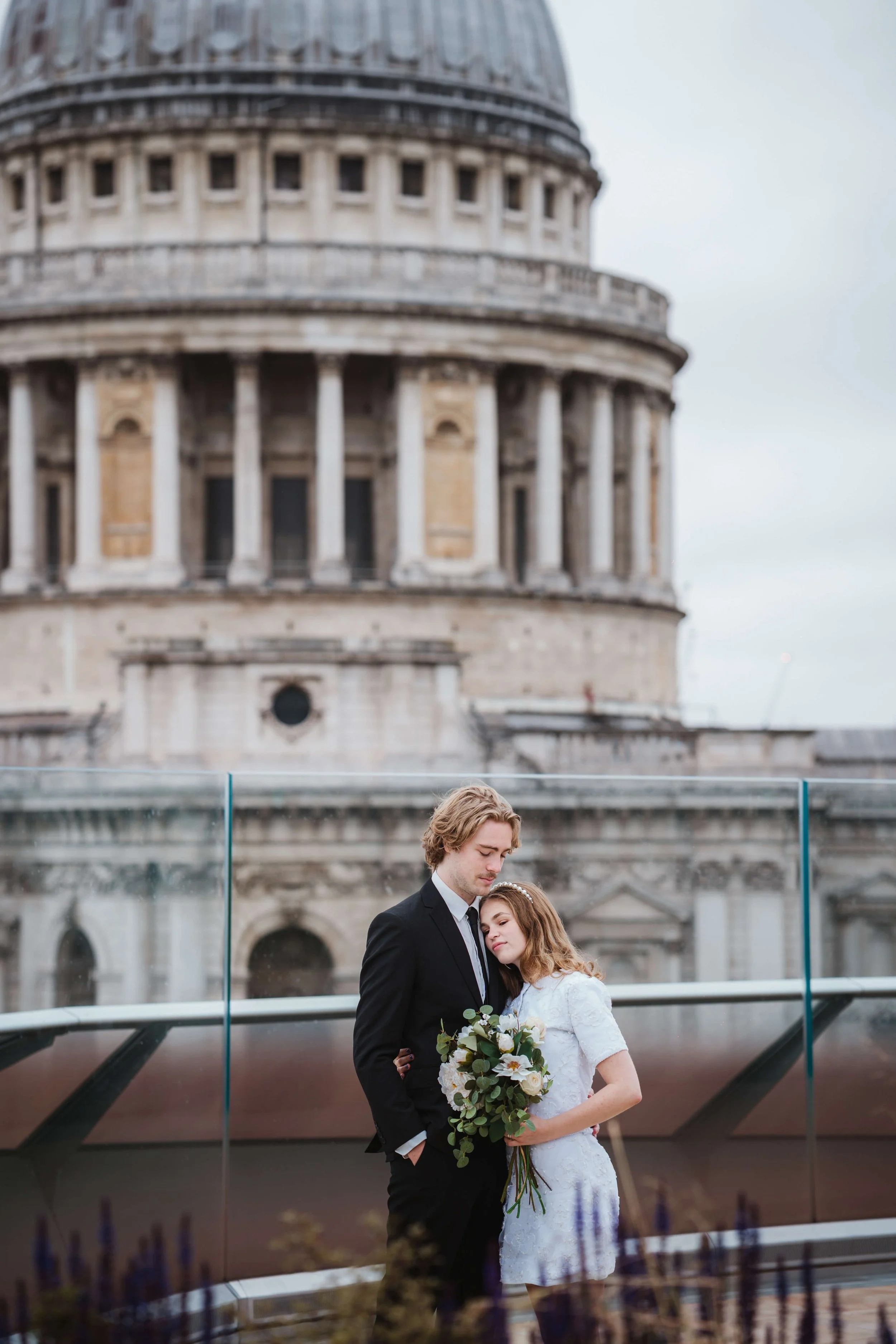 bride nestles head on grooms shoulder on roof top of one new change opposite St Pauls Cathedral 