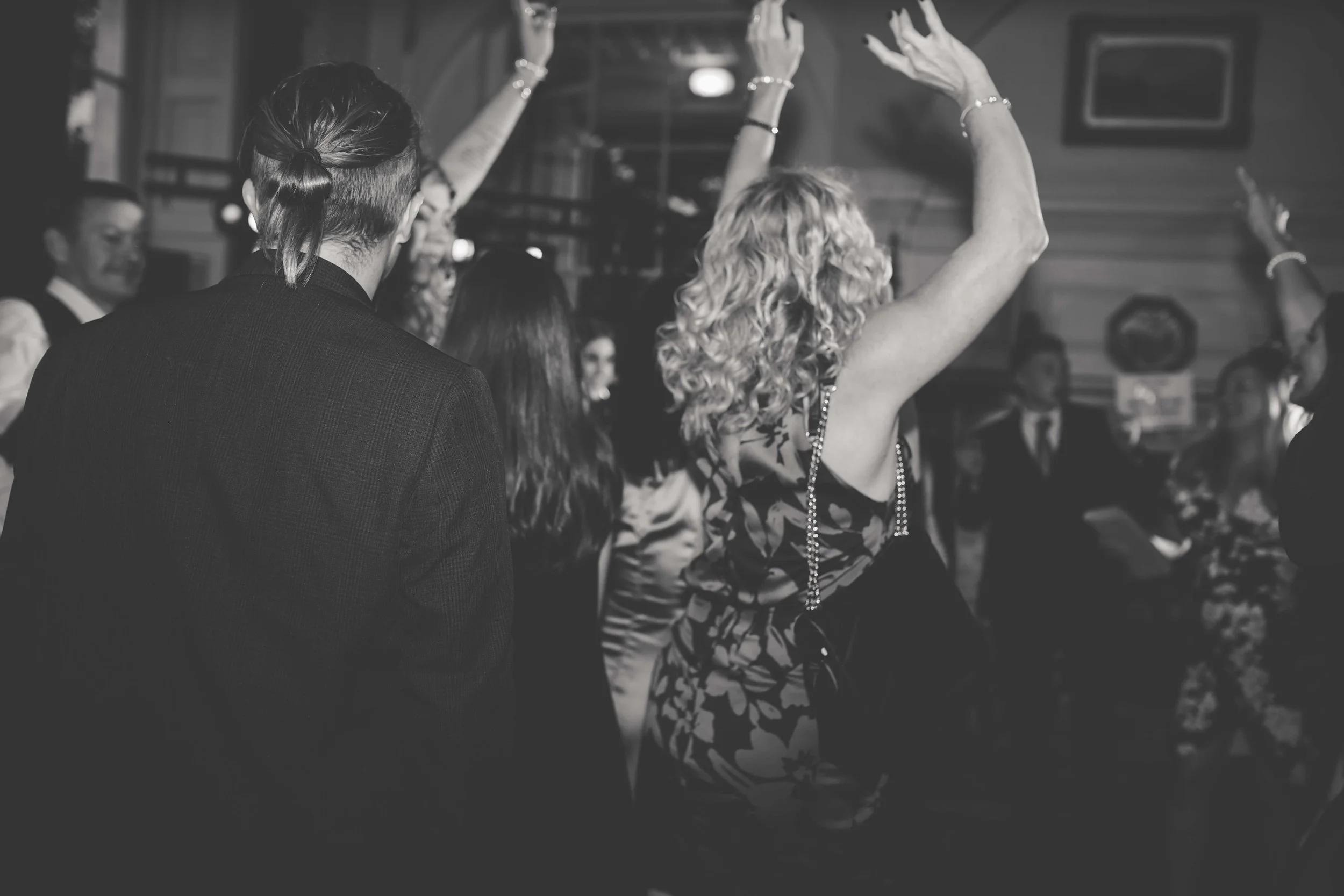 People dancing at an indoor event, with a woman in a patterned dress with curly hair dancing with her arms raised.