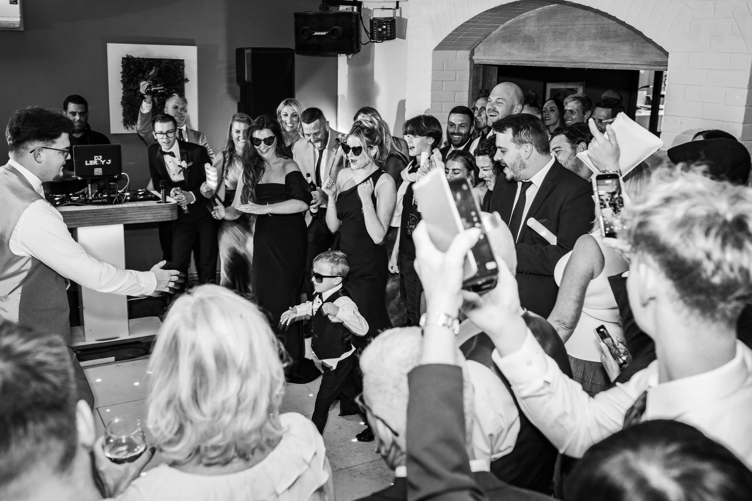 People dancing and enjoying a lively celebration at a wedding or party, with a DJ in the background.