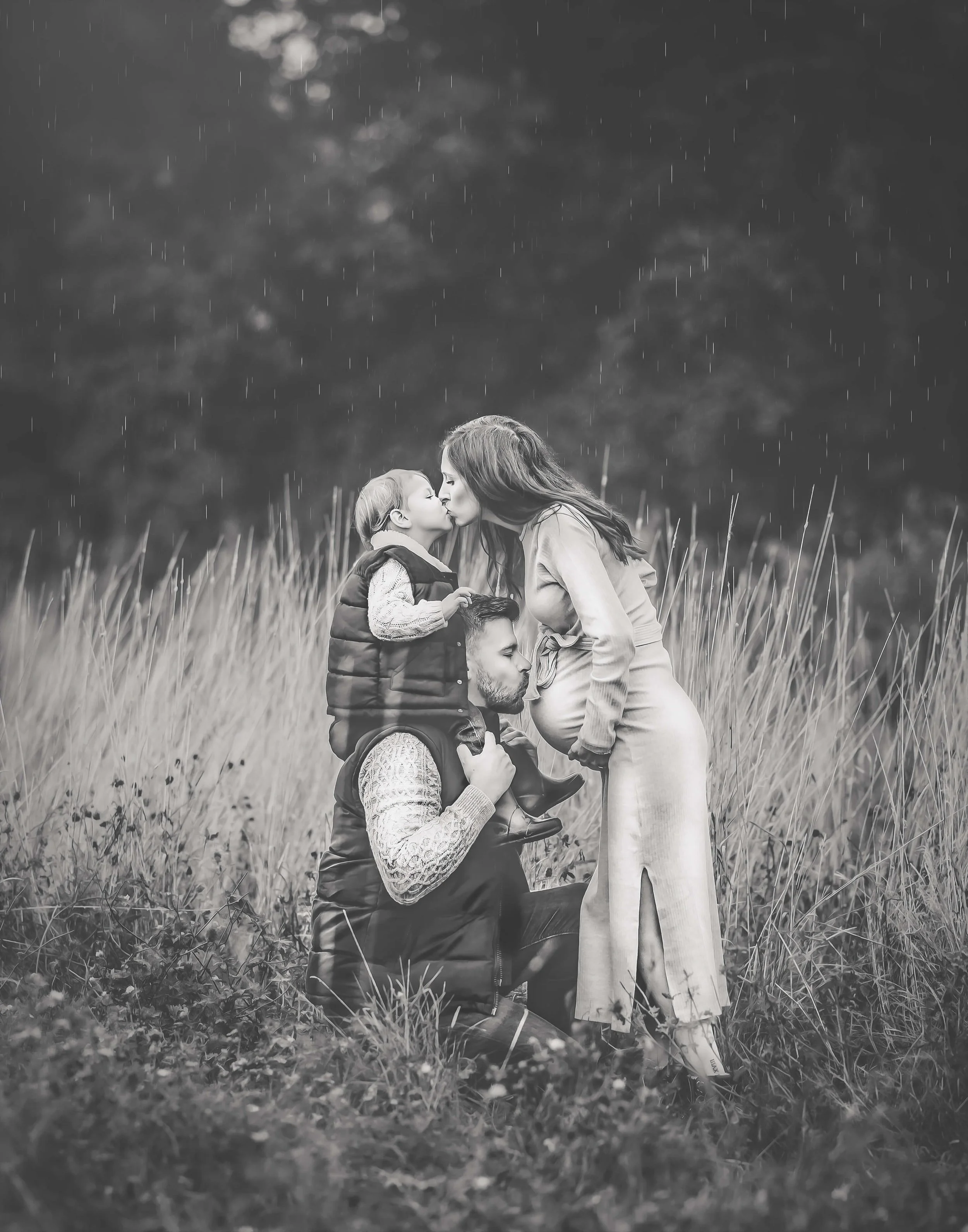 pregnant mother kissing child on dads shoulders whilst dad kisses mums bump