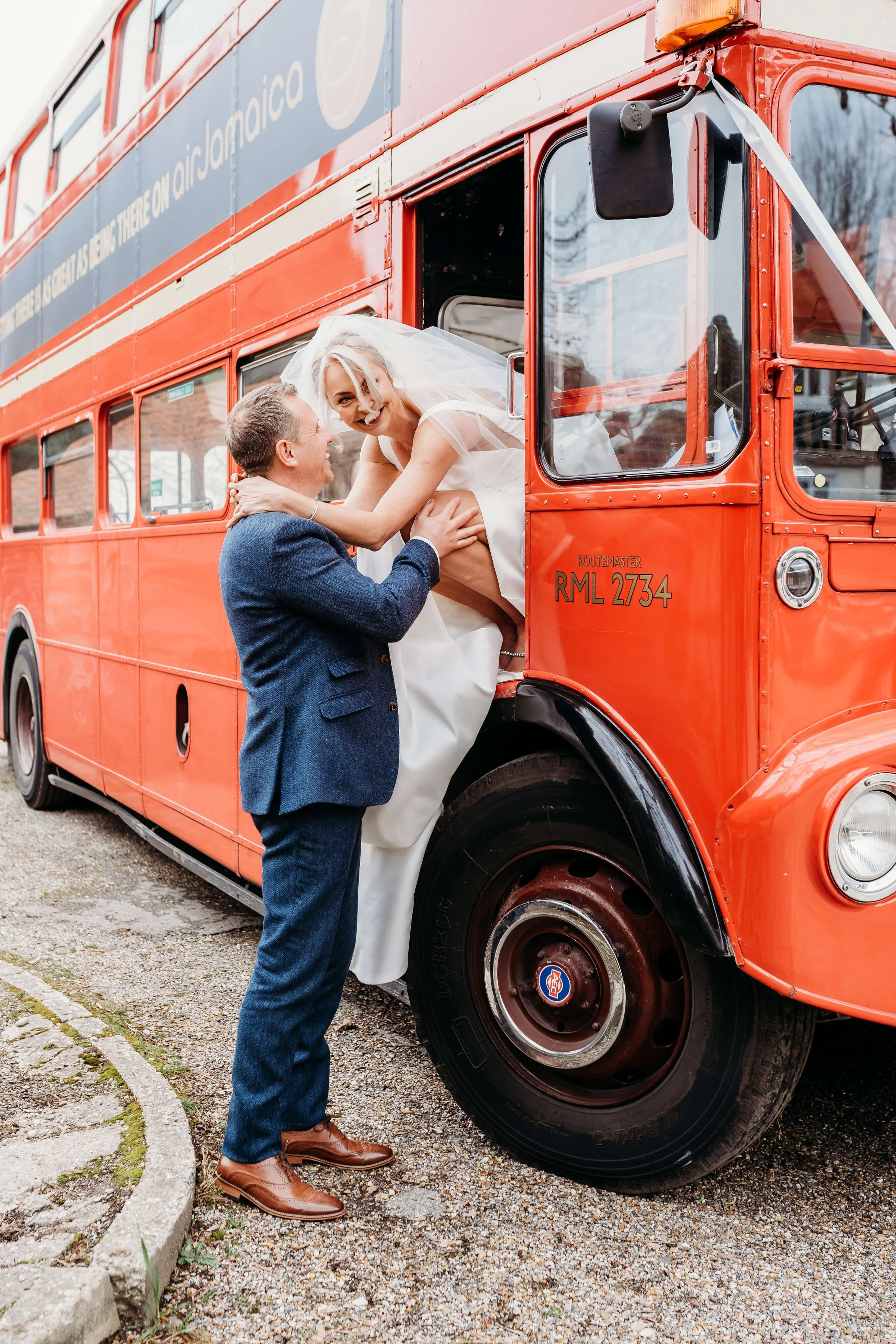 A groom lifting his bride into a red double-decker bus on a city street, wedding celebration, outdoor photo