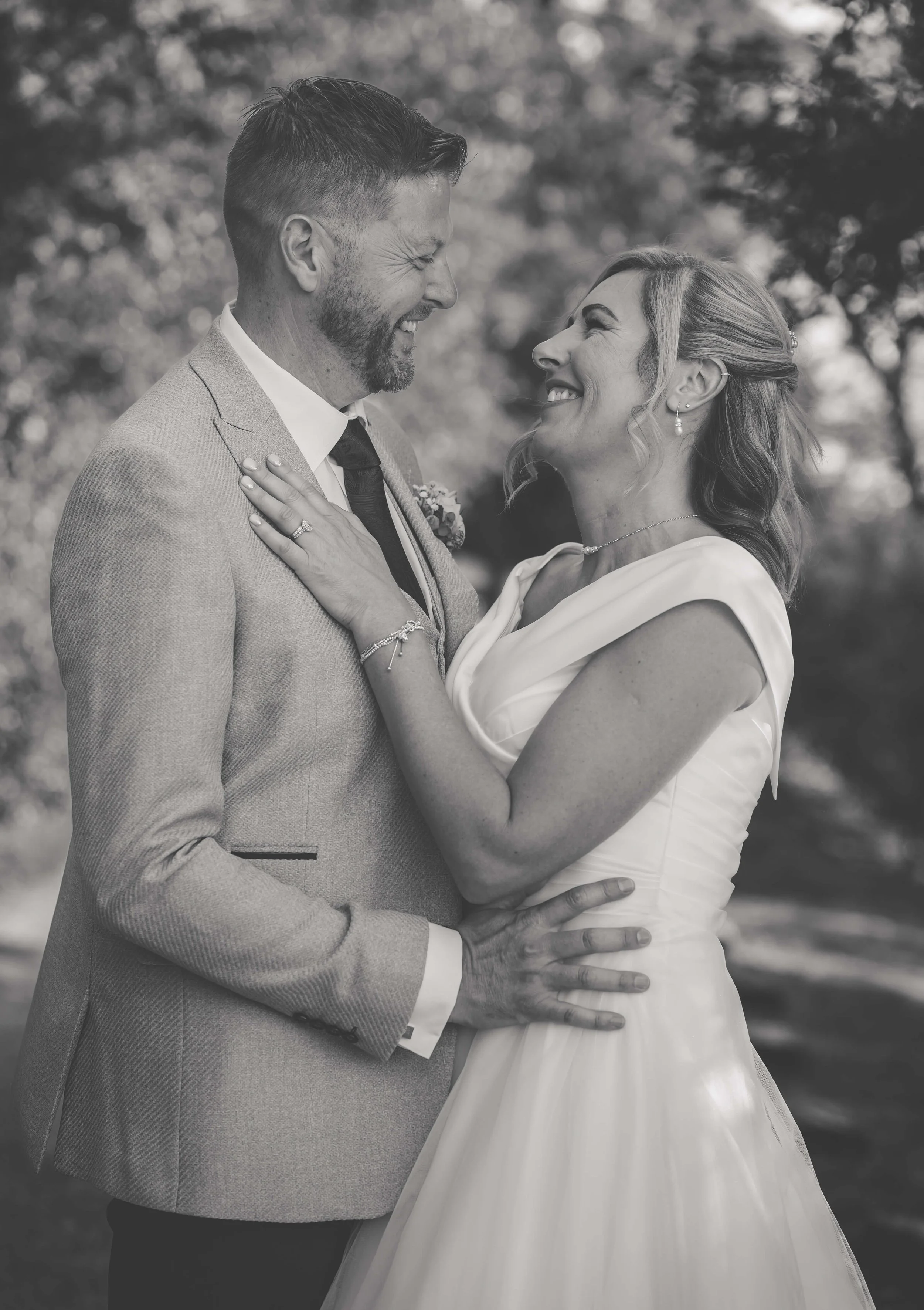 A happy couple, the man in a suit and the woman in a wedding dress, gazing into each other's eyes outdoors.