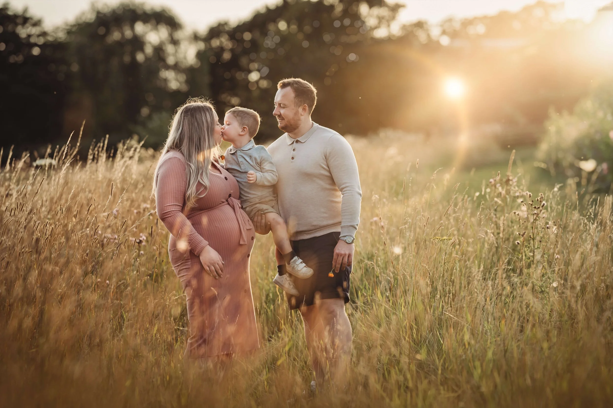 golden hour maternity photograph of family son kissing mum 