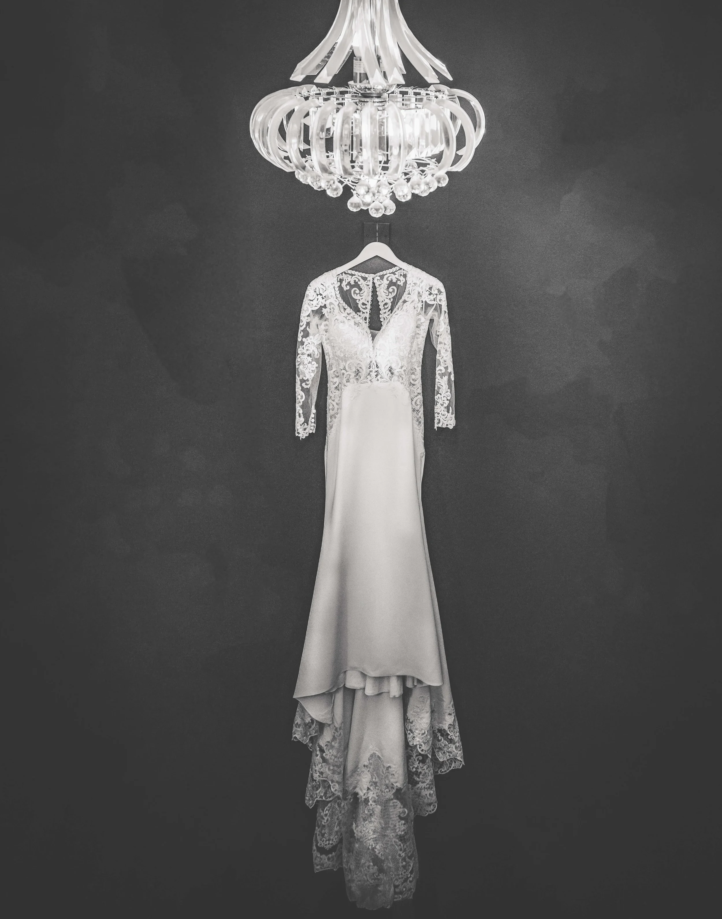 Artistic photograph of bridal dress hanging up using light from chandelier in black and white