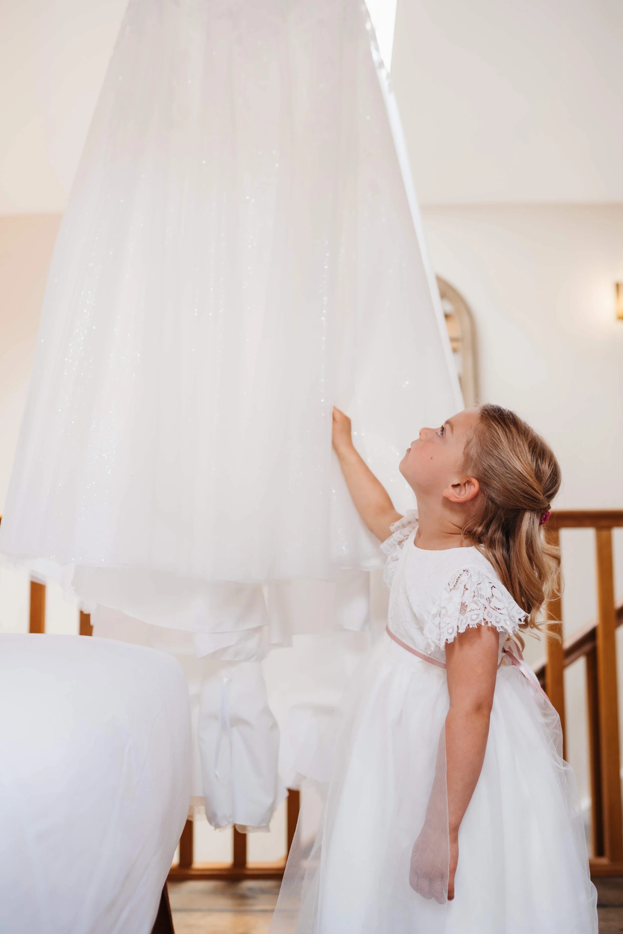 A young girl dressed in a white dress looks up at a hanging white dress with glittery sparkles.