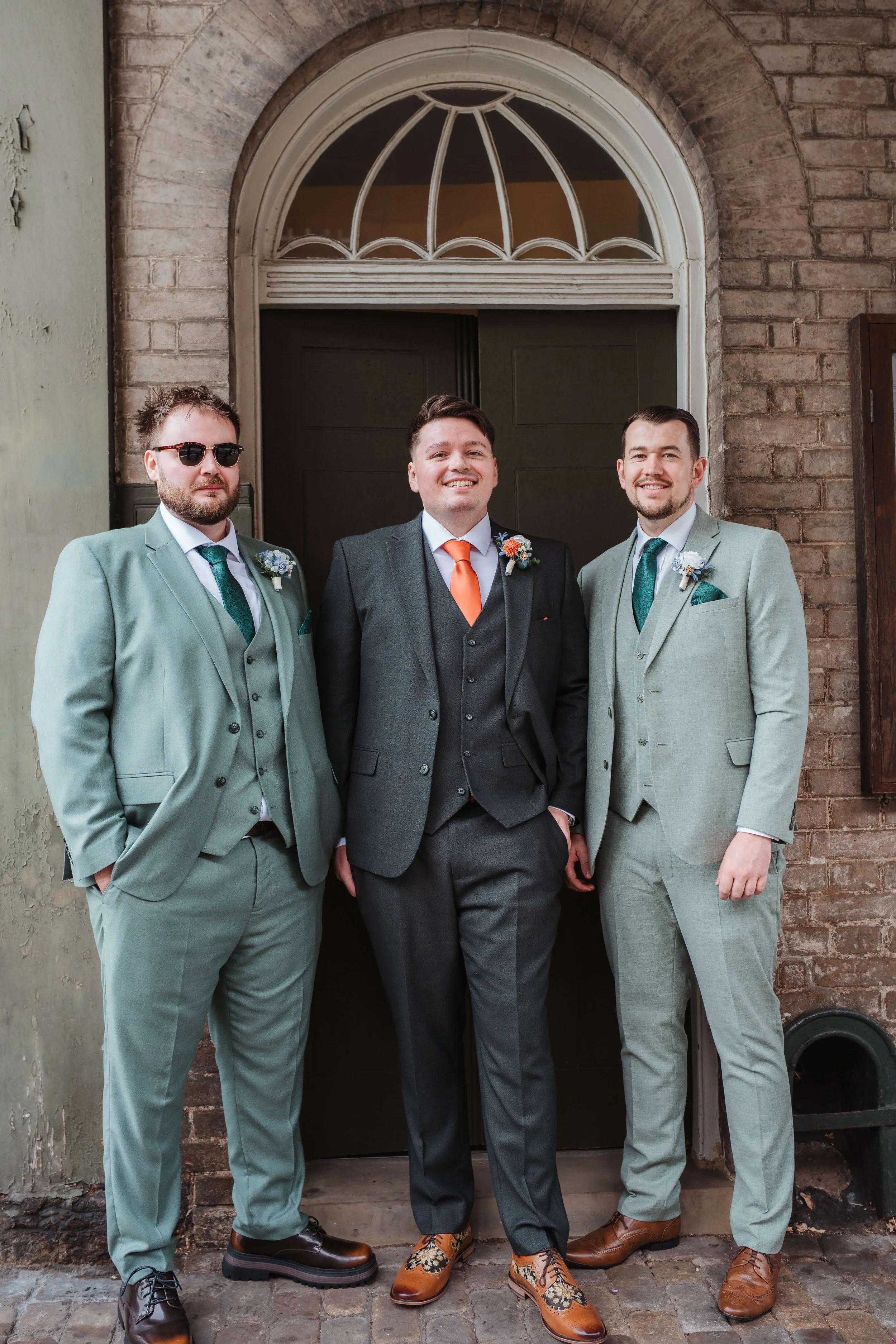 Three men in suits standing outside a building door, smiling.