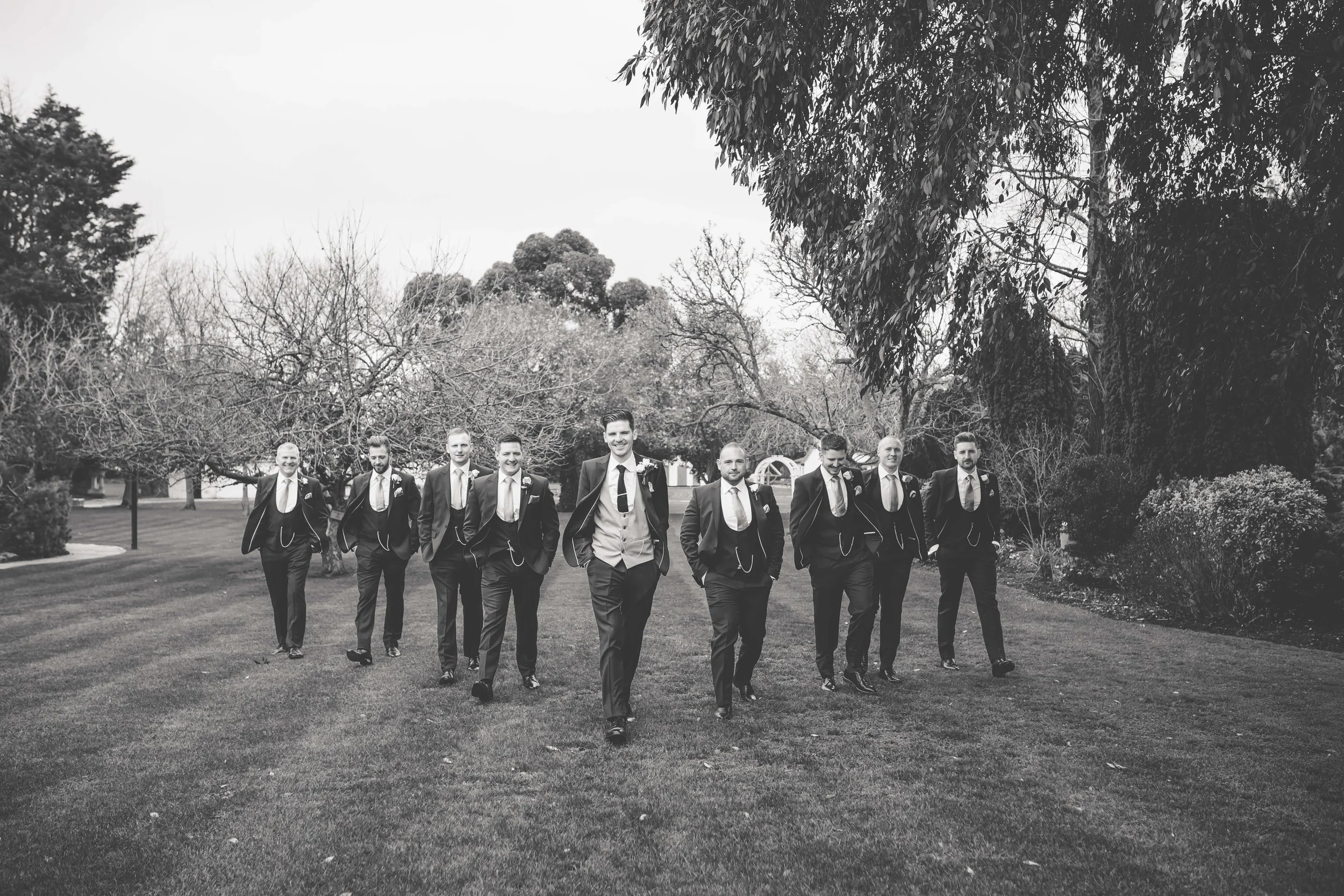 black and white photo of groom and groomsmen walking in unison in the grounds of wedding reception Ye Old Plough in Essex