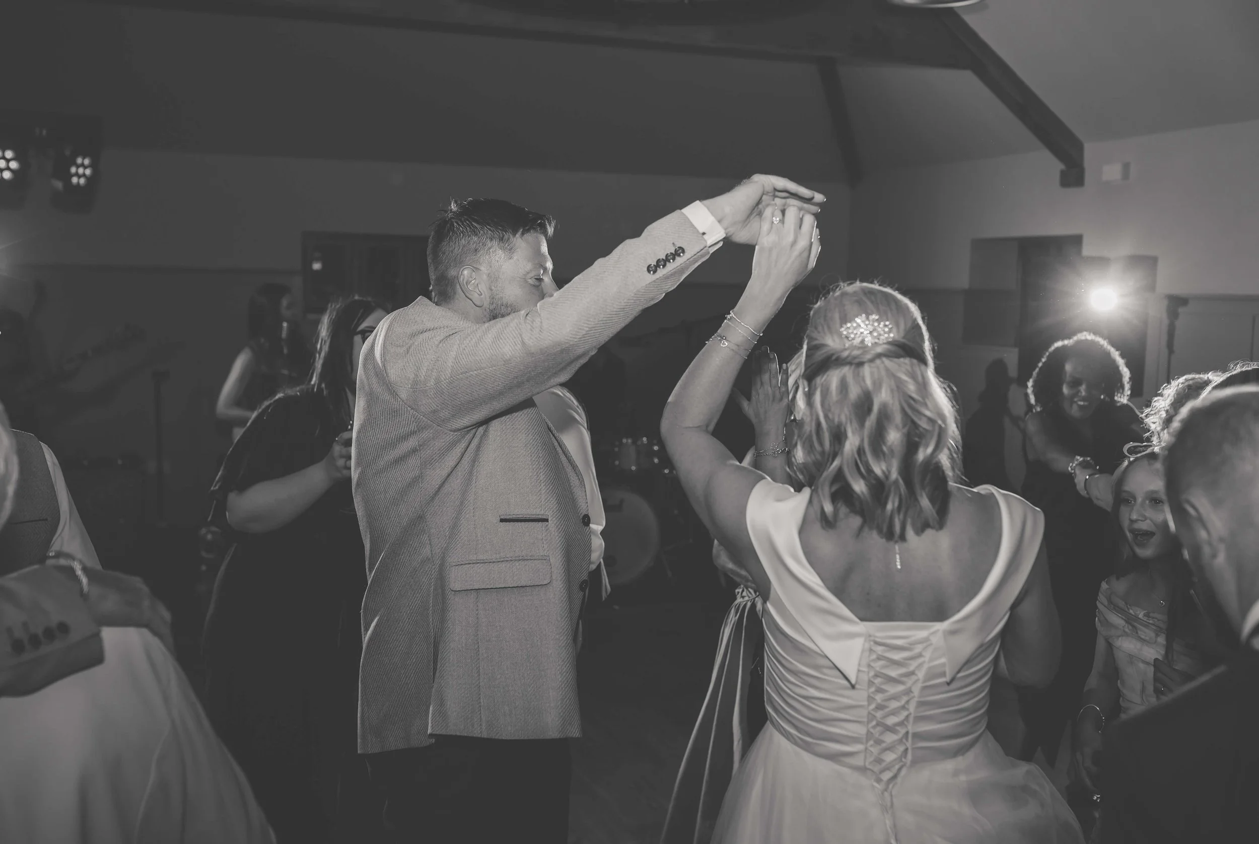 Couple dancing at a wedding reception, surrounded by guests in a ballroom with dim lighting.
