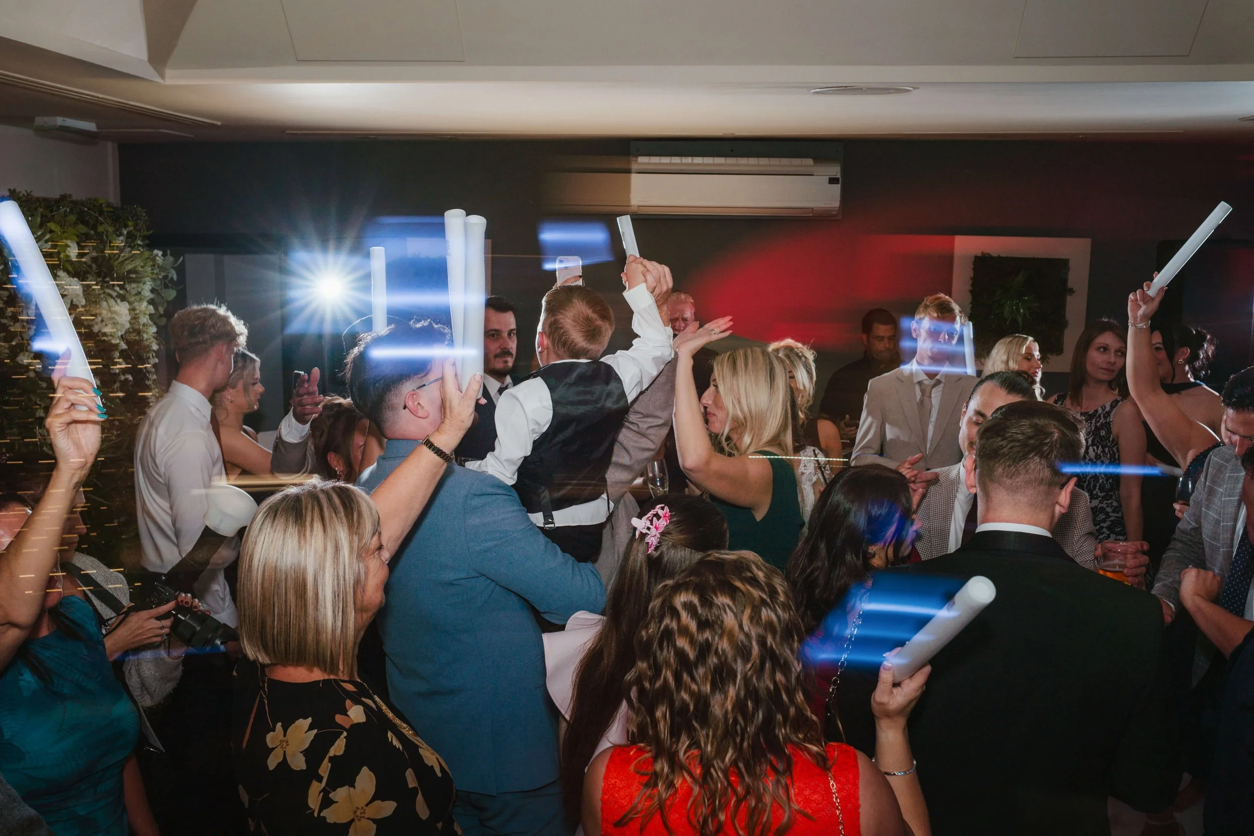 People dancing at a party with glowing foam sticks and colorful lights.